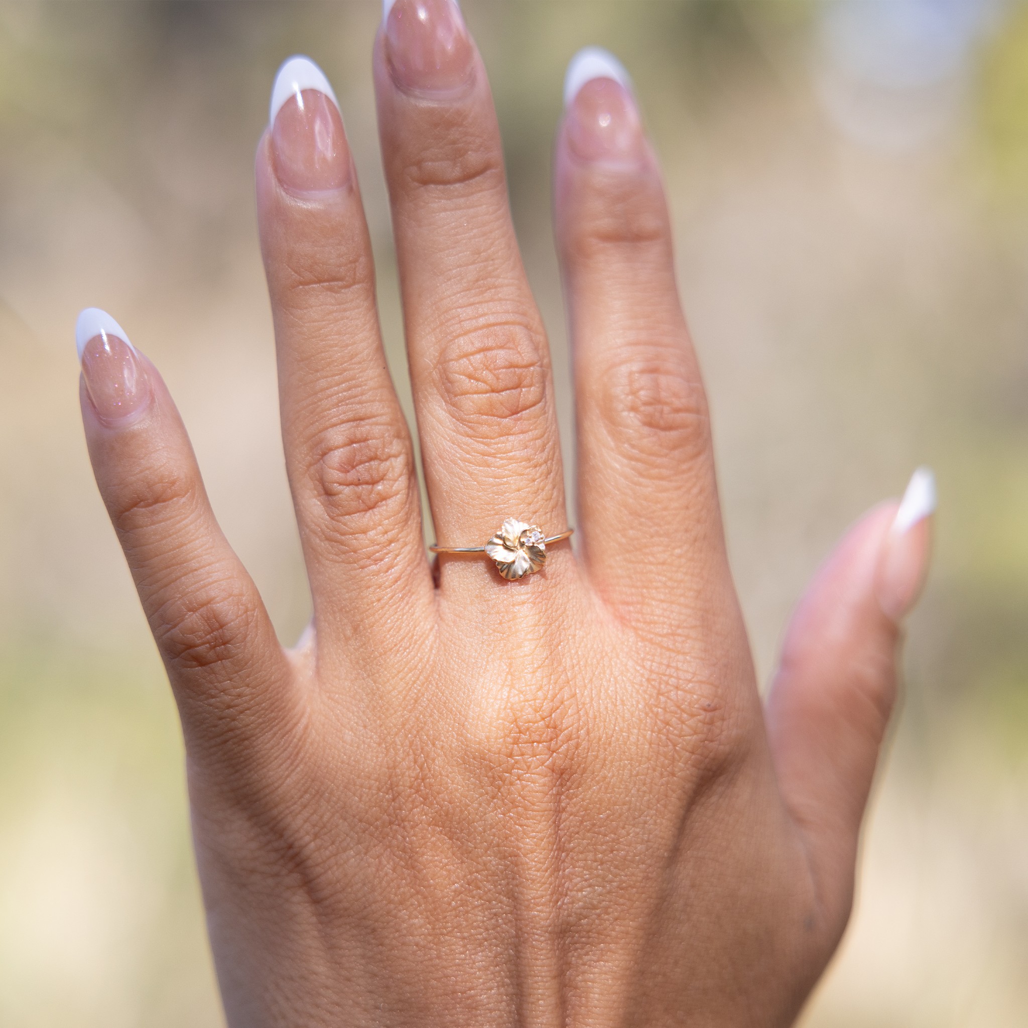 8mm Hawaiian Gardens Hibiscus Ring in 14k Yellow Gold with Diamonds on hand held up against blurred nature background