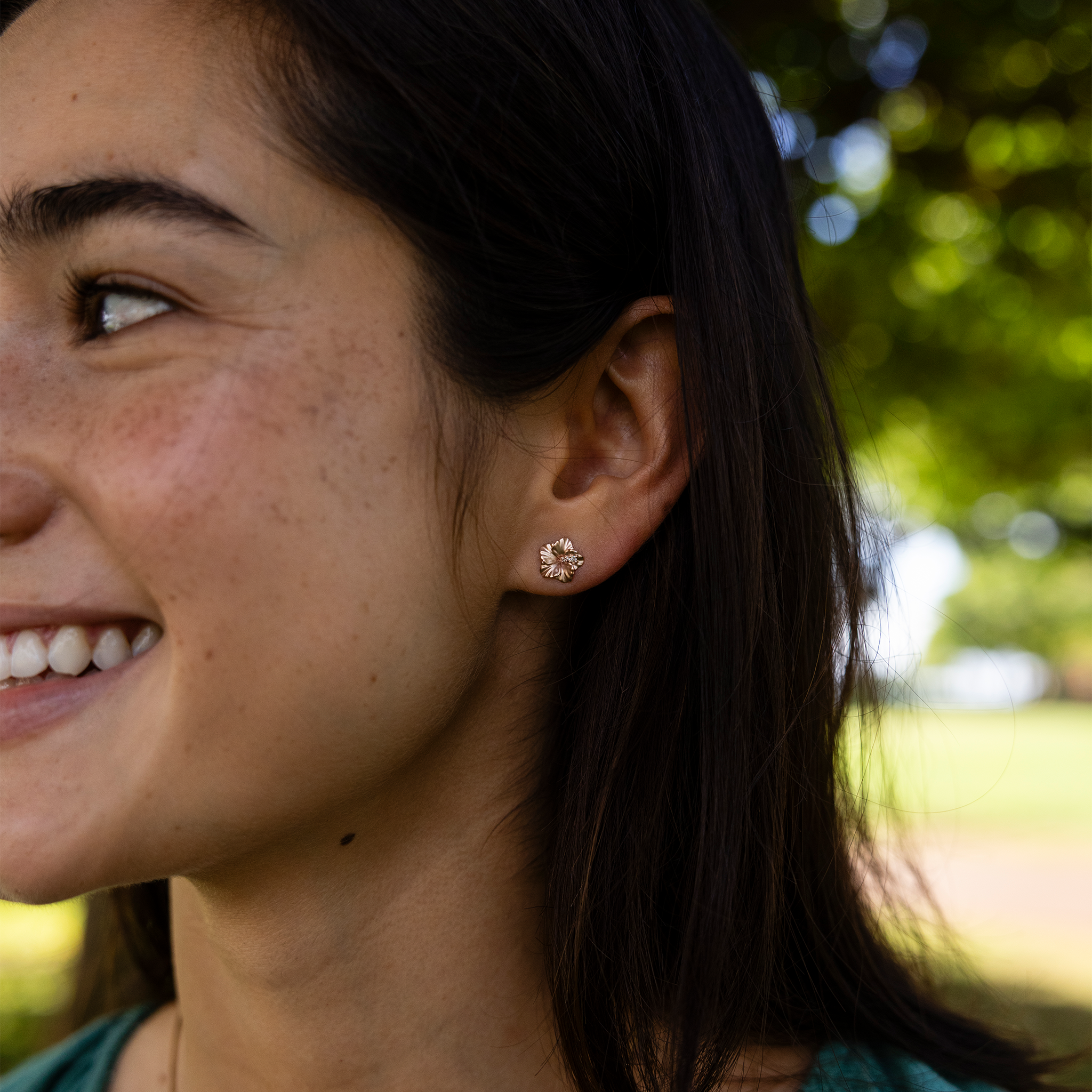 Close up of a woman at at park wearing 9.5mm Diamond Hibiscus Earrings in 14k Rose Gold