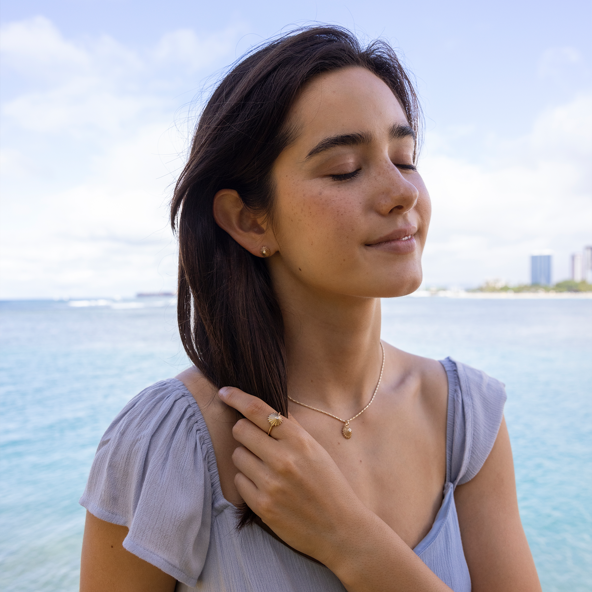 Woman by the ocean wearing 12mm ʻOpihi Ring, Pendant and Earrings in Gold with Diamonds