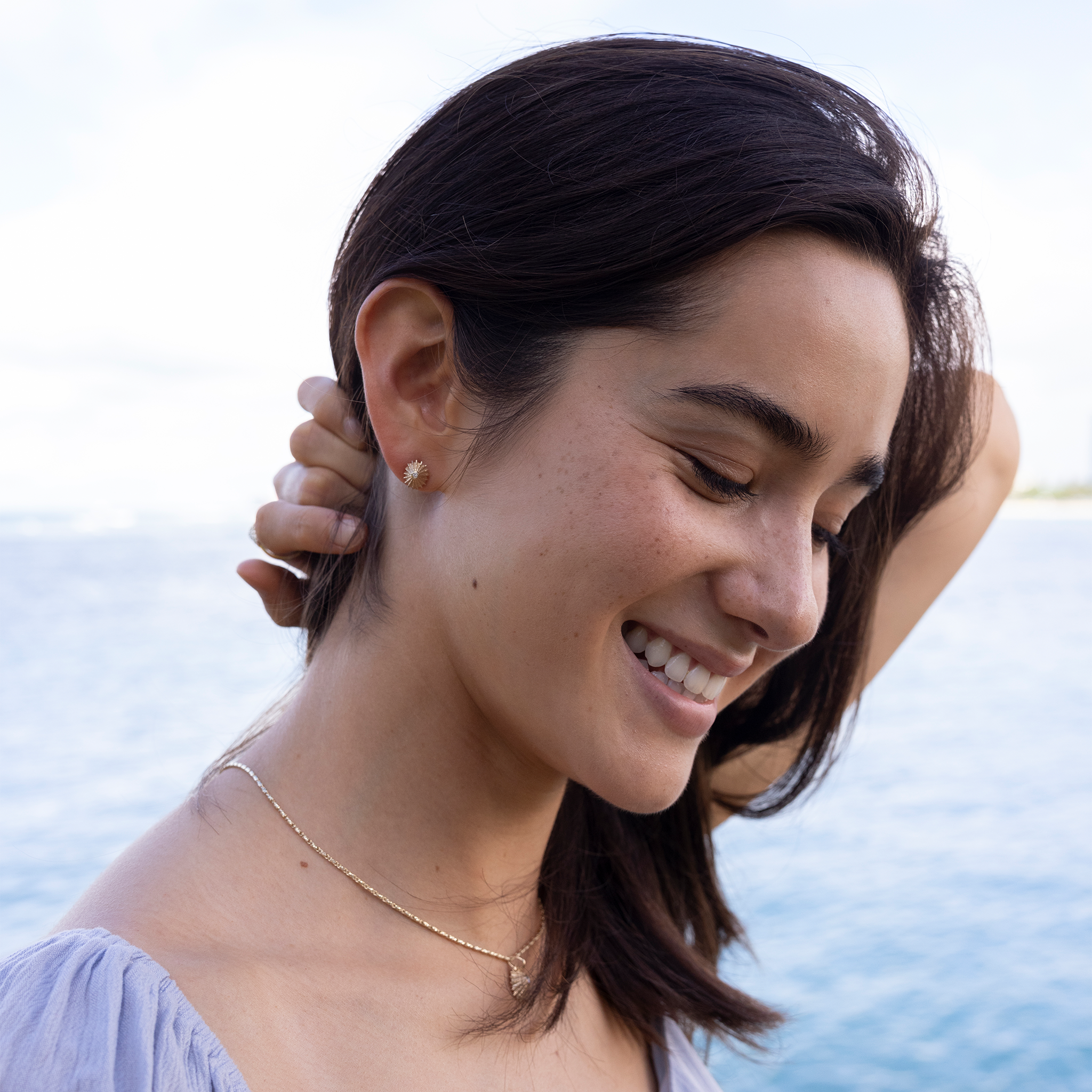 Close up of a woman by the ocean wearing 10mm ʻOpihi Earrings and Pendant in Gold with Diamonds