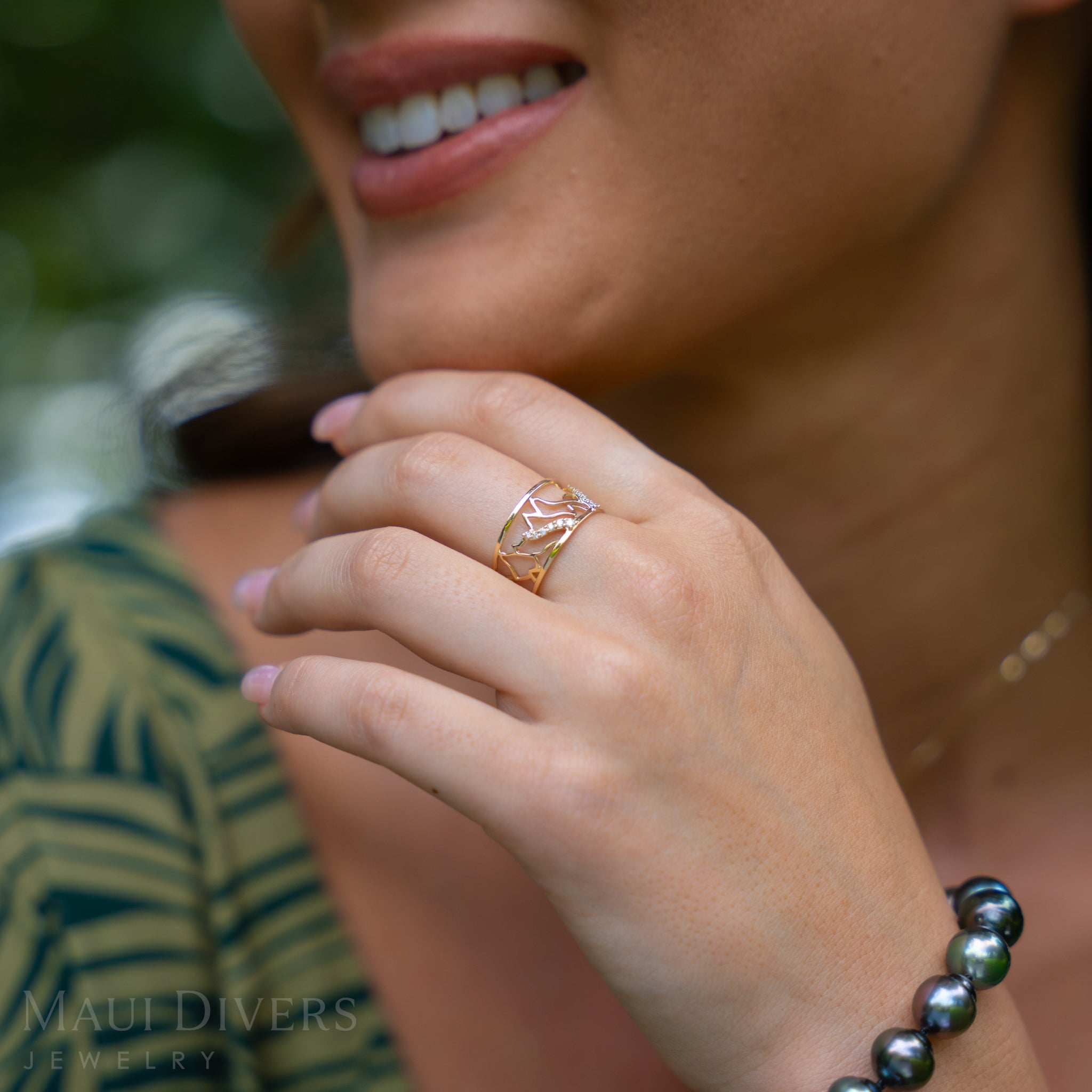 Close-up of a hand wearing a 10mm Koʻolau Waterfall Ring in Gold with Diamonds with a blurred background