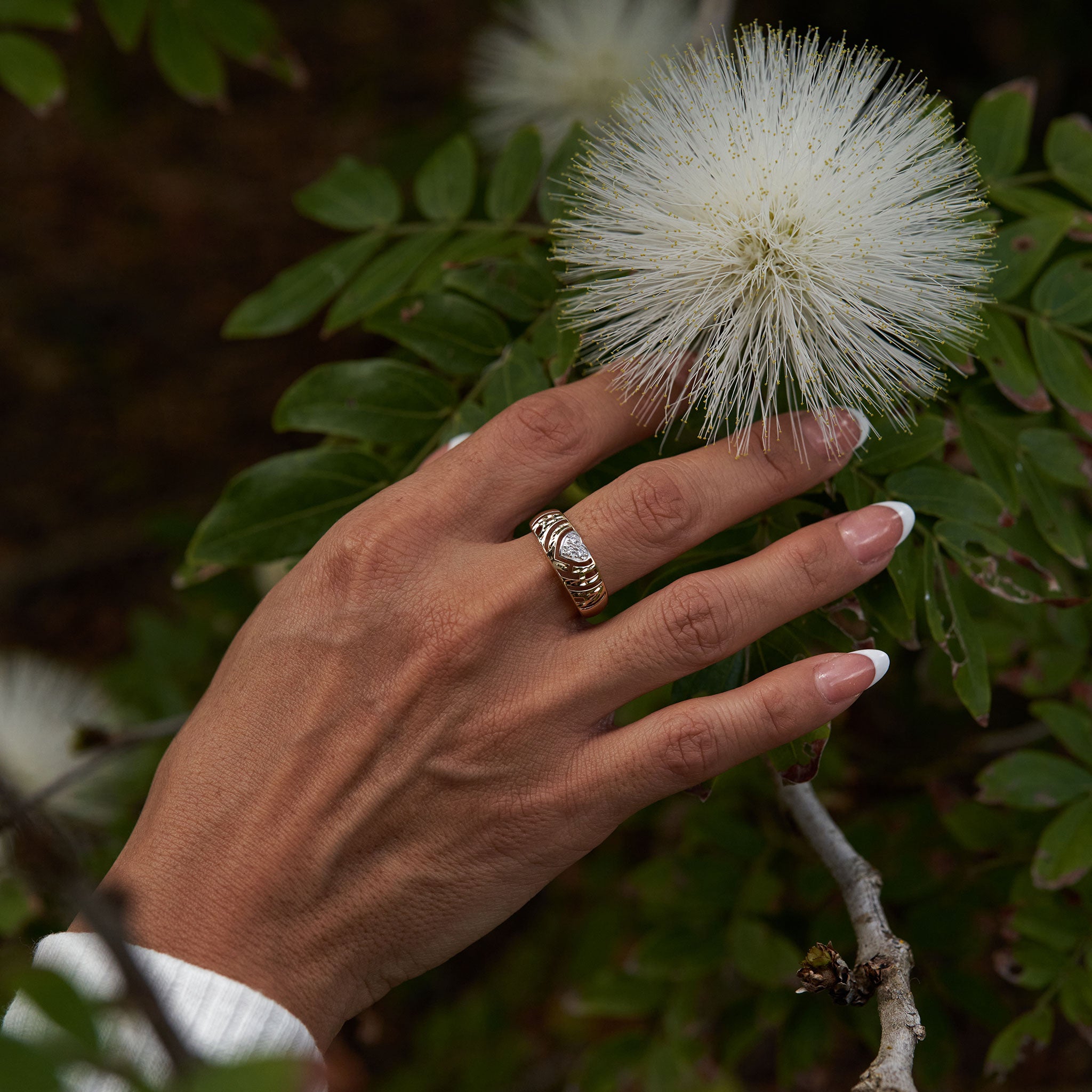 8mm Aloha Heart Ring in Gold with Diamonds on a hand against leaves and white flowers