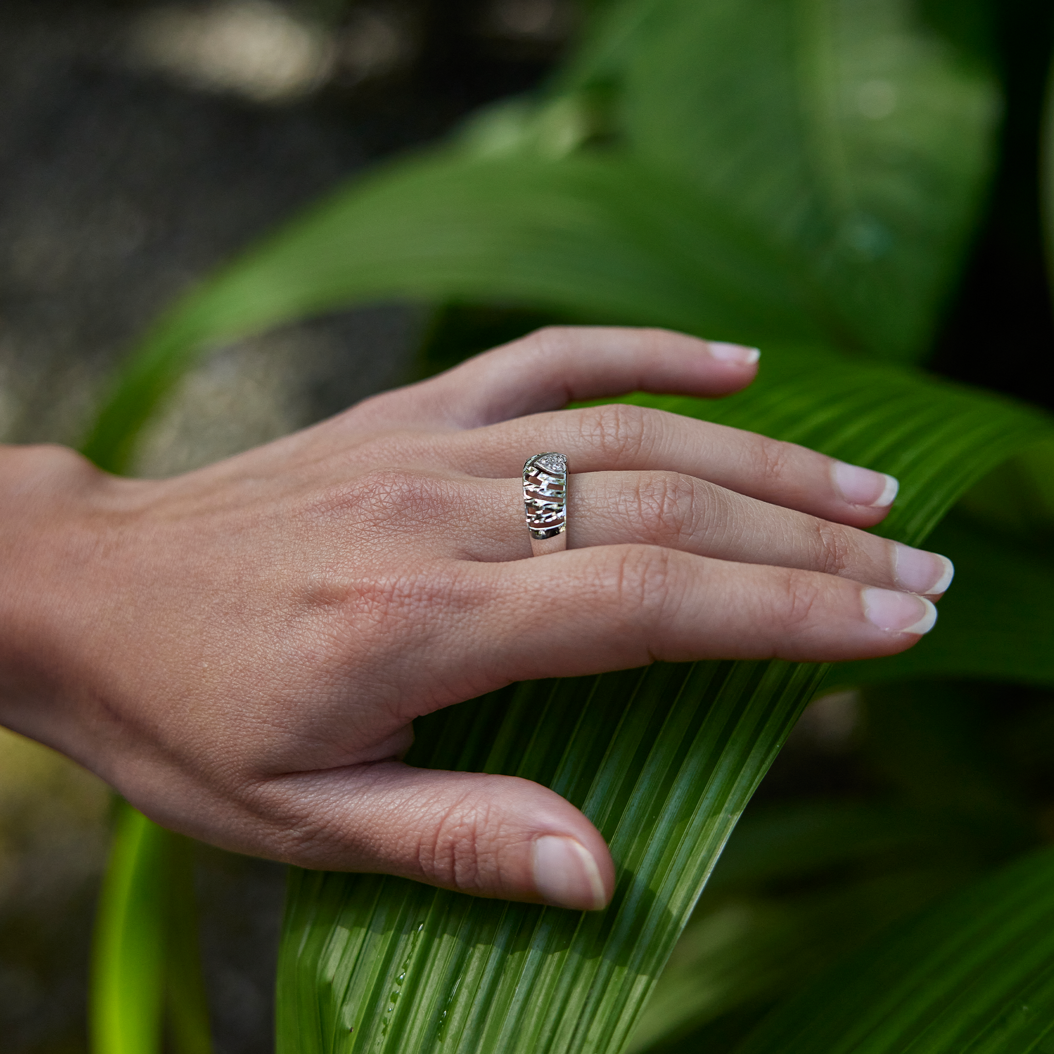 Close up of 8mm Aloha Heart Ring in White Gold with Diamonds on a hand over a large green leaf