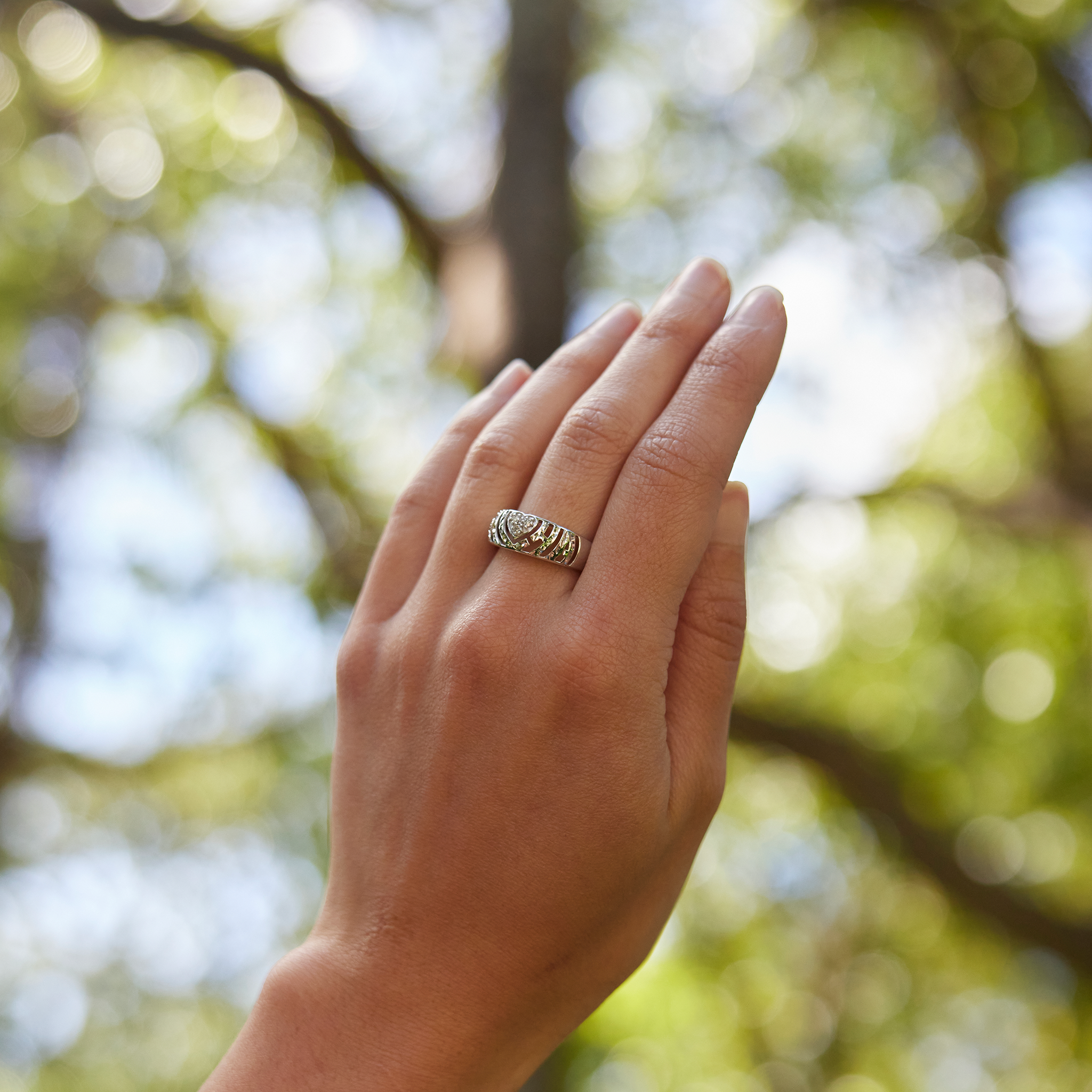 Close up of 8mm Aloha Heart Ring in White Gold with Diamonds on a hand over a blurred nature background