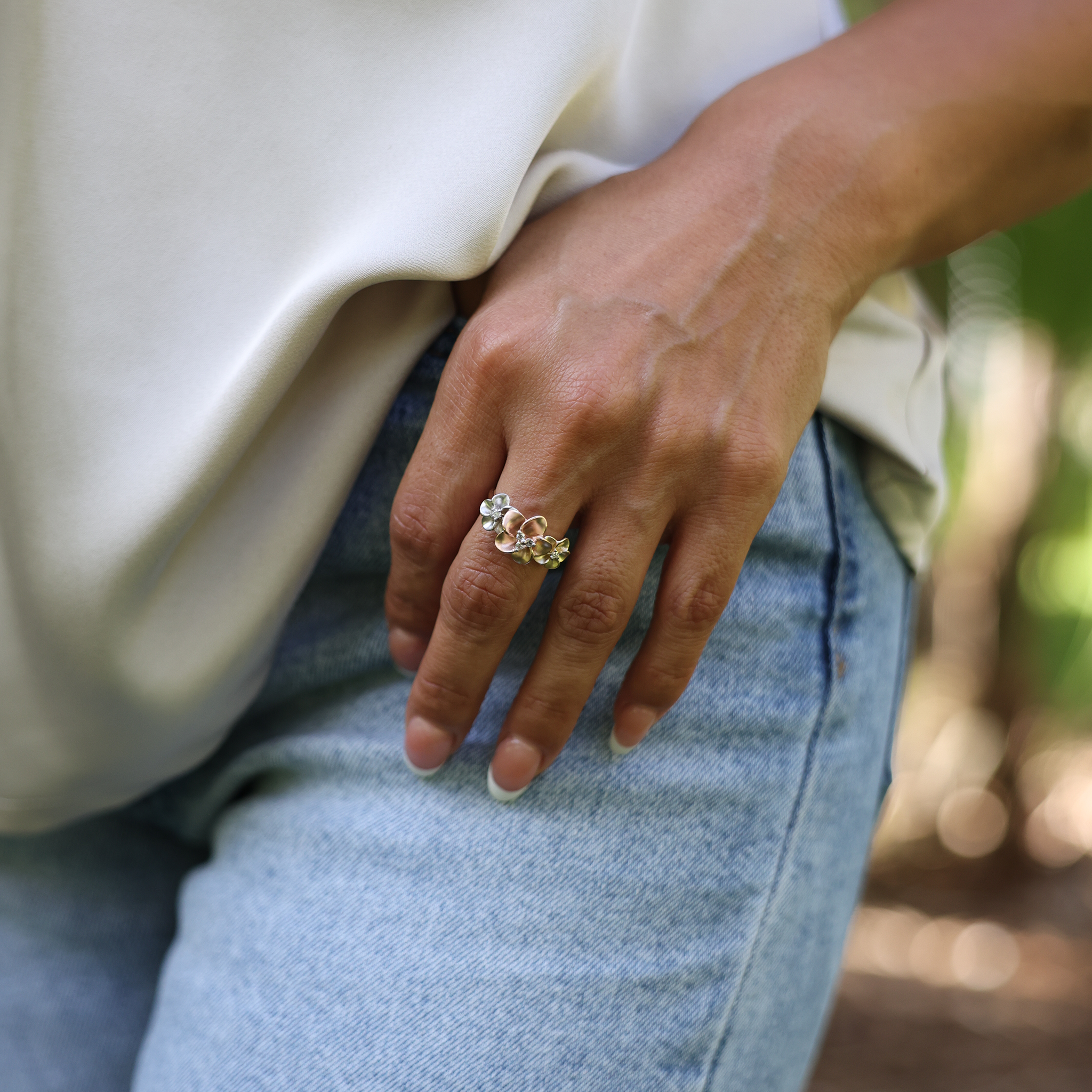 12mm Three Plumeria Ring in Tri Color Gold with Diamonds on a hand against jeans and a white top