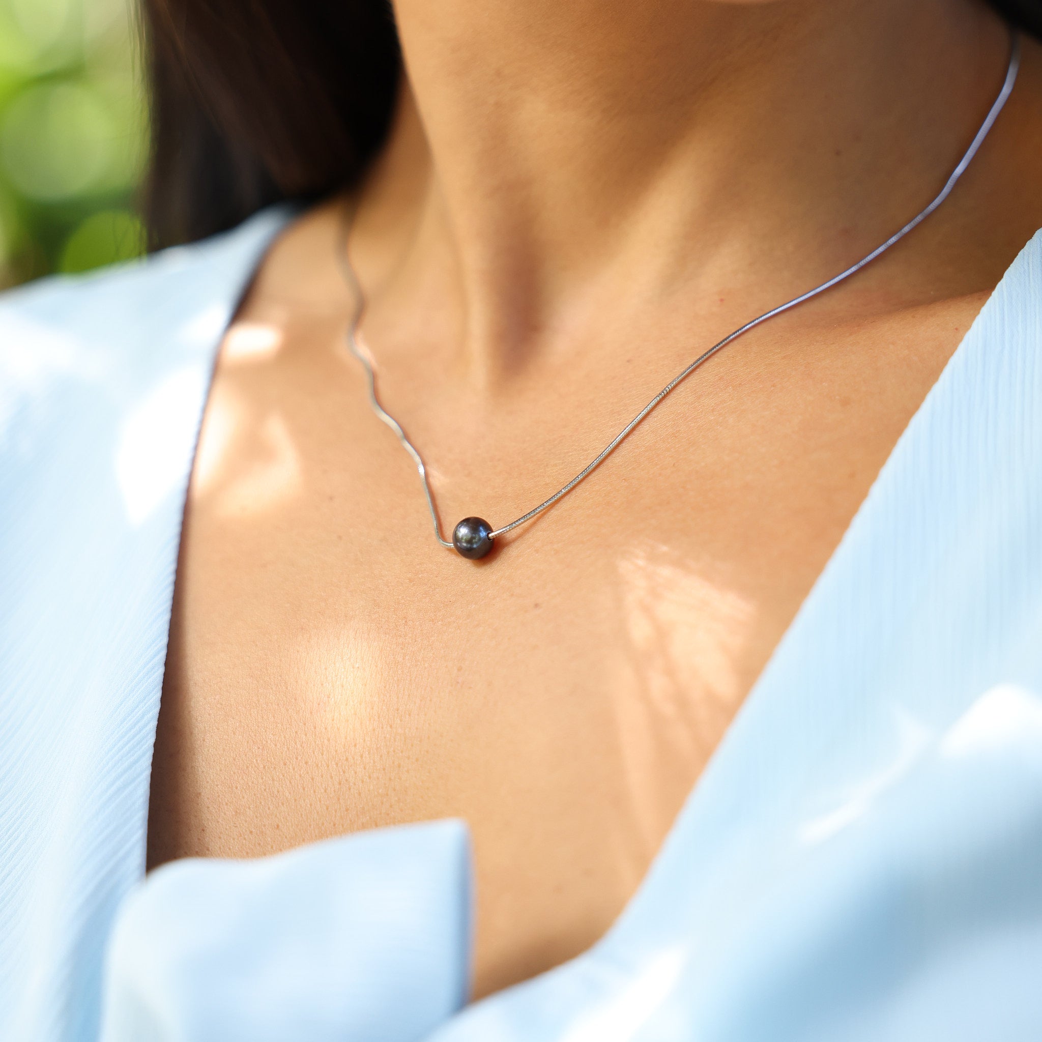 Close up of a Tahitian Black Pearl slider Necklace in Sterling Silver on a woman's neckline outdoors