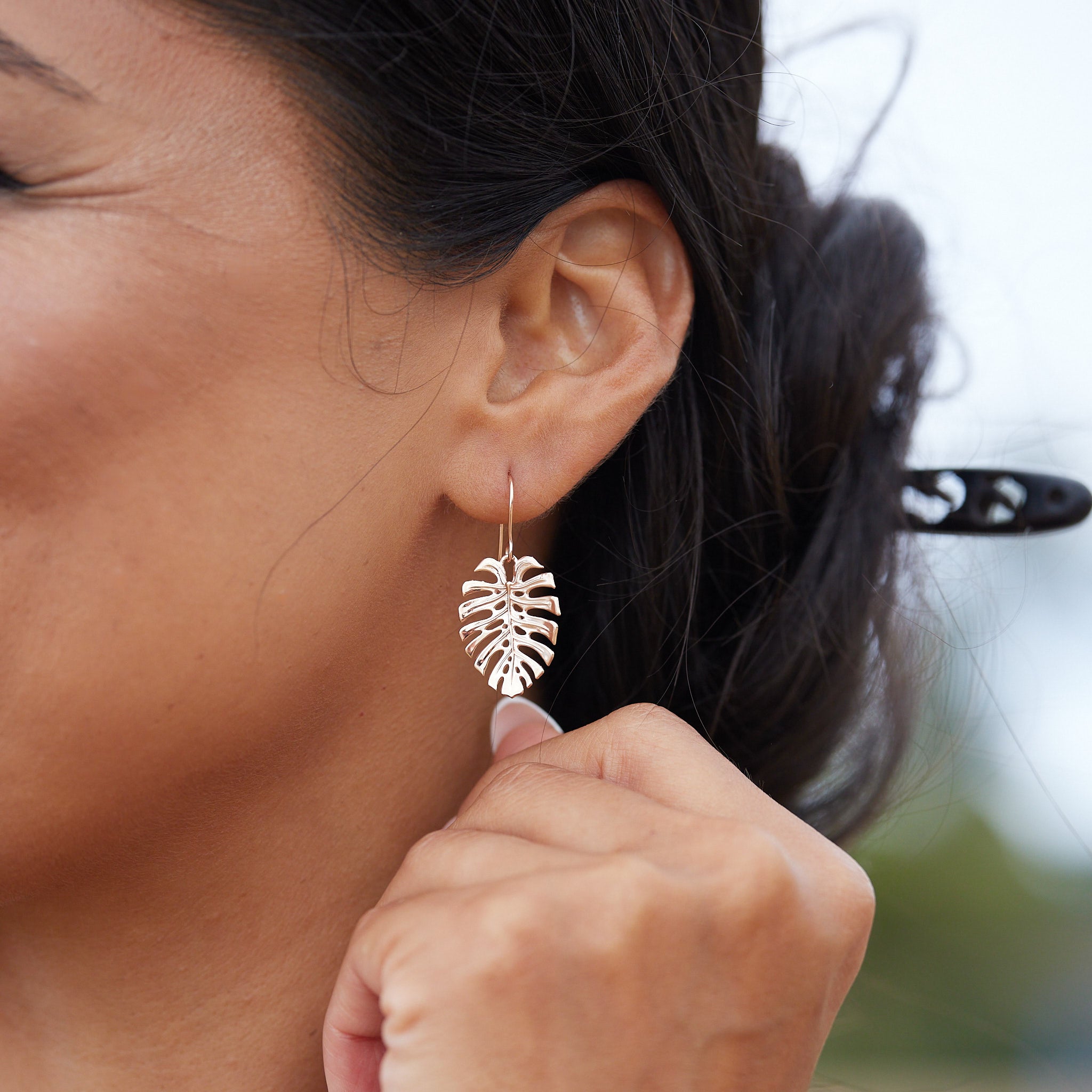 A woman's ear with 23mm Monstera Earrings in Rose Gold outdoors