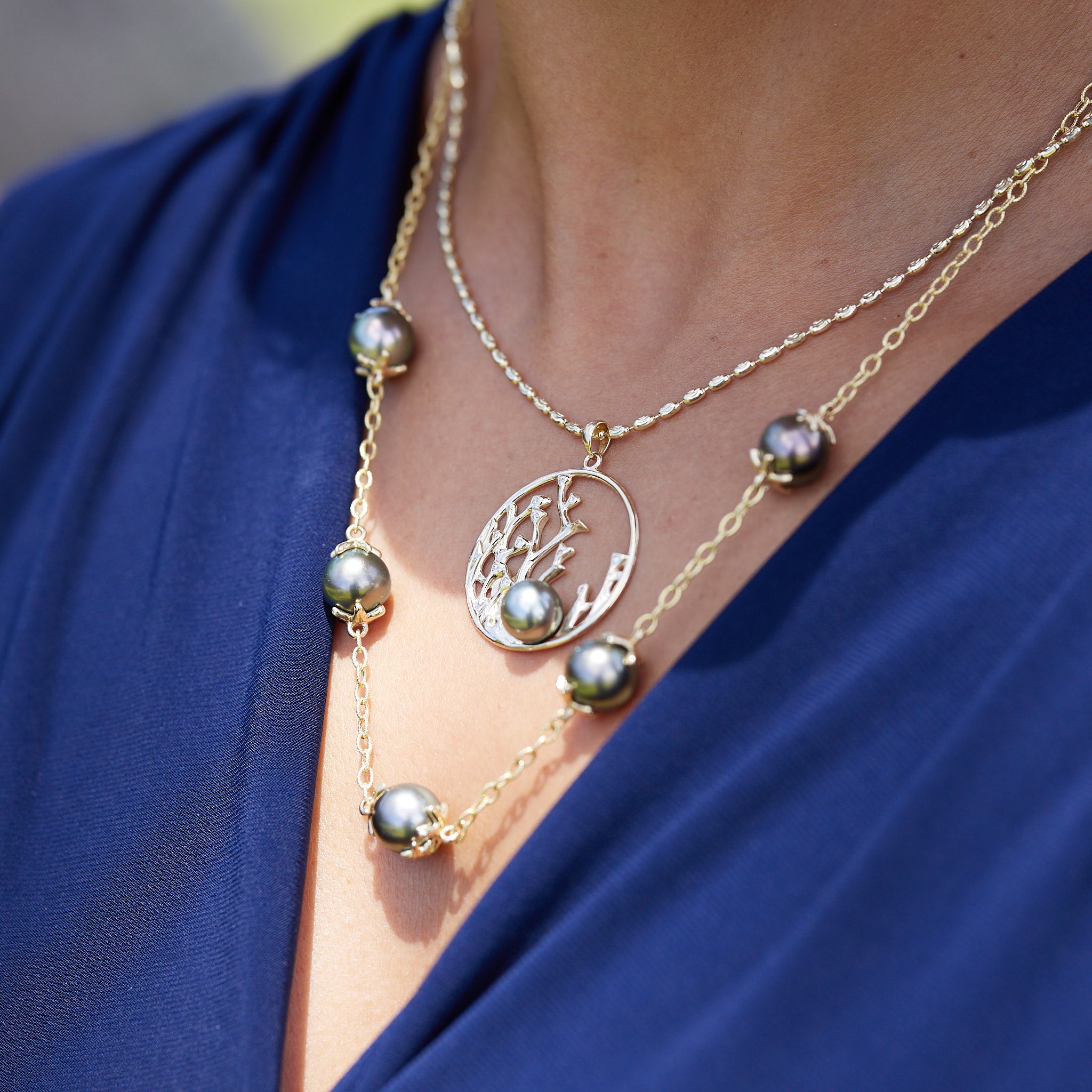A woman wearing a 1.8mm Ovalina Chain in Gold with a pendant layered with a pearl necklace outdoors