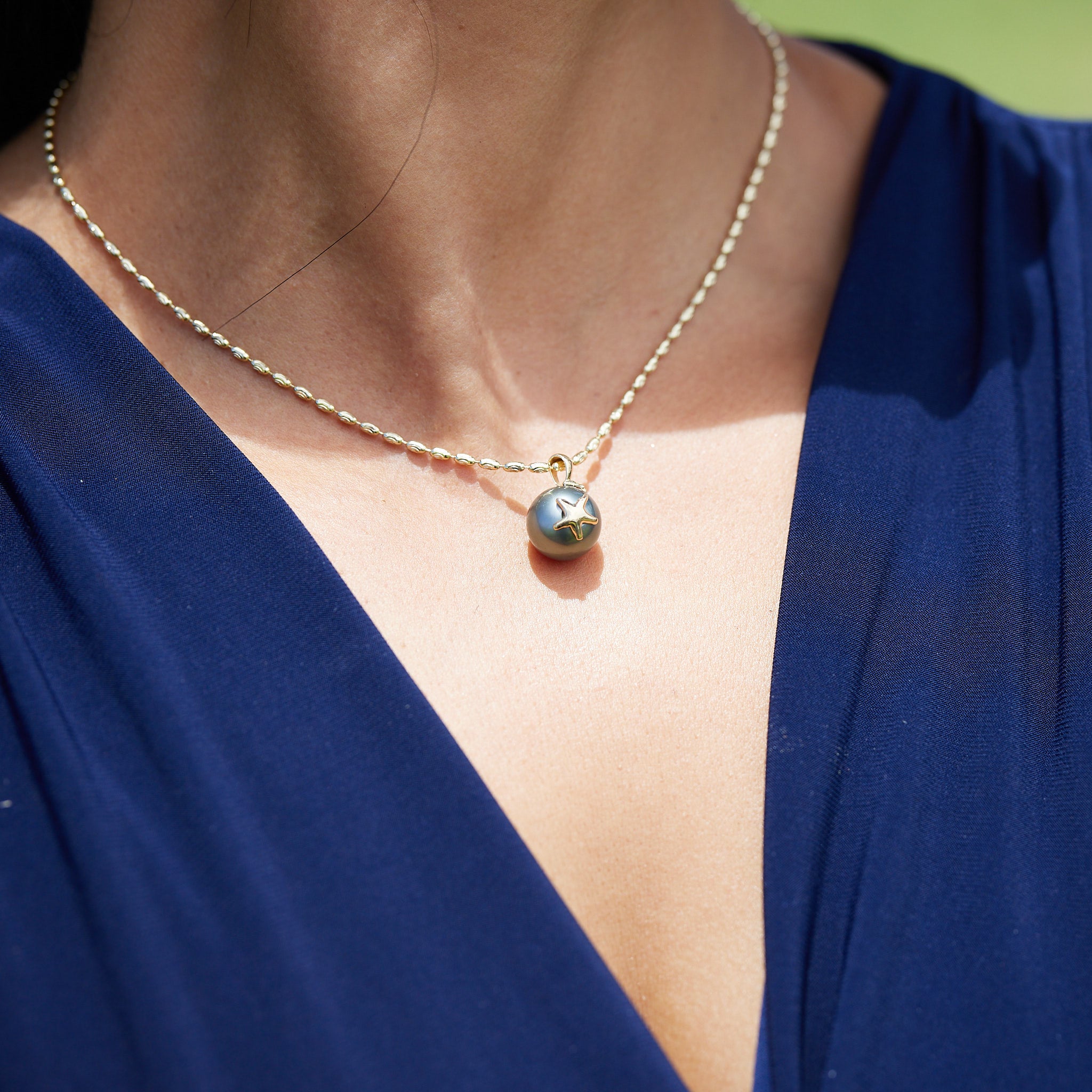 Close up of a woman wearing a 1.8mm Ovalina Chain in Gold with a pearl pendant outdoors