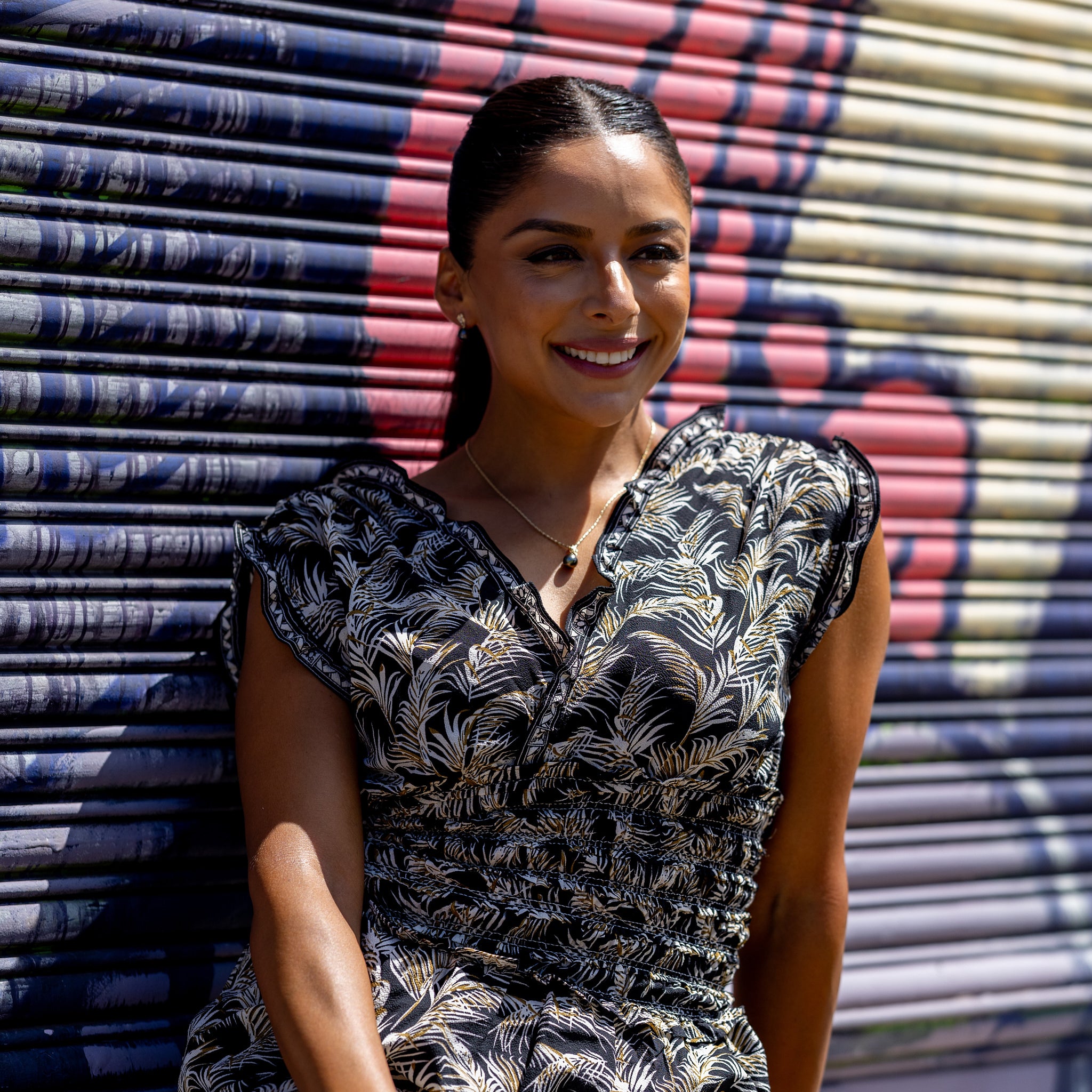 Woman in a black patterned dress wearing the Living Heirloom Tahitian black pearl pendant on a raso chain with a graffiti backdrop