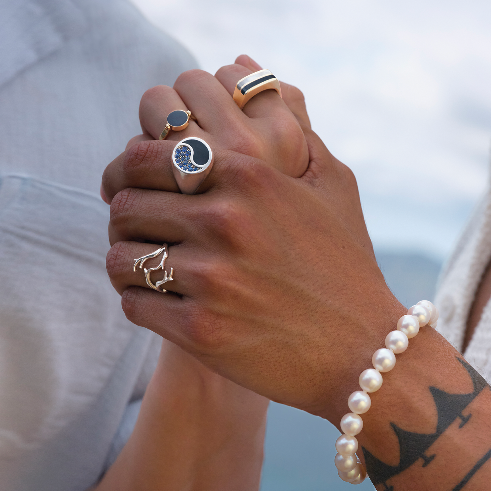 Hands embracing wearing multiple Black Coral Rings in Gold with Mother of Pearl