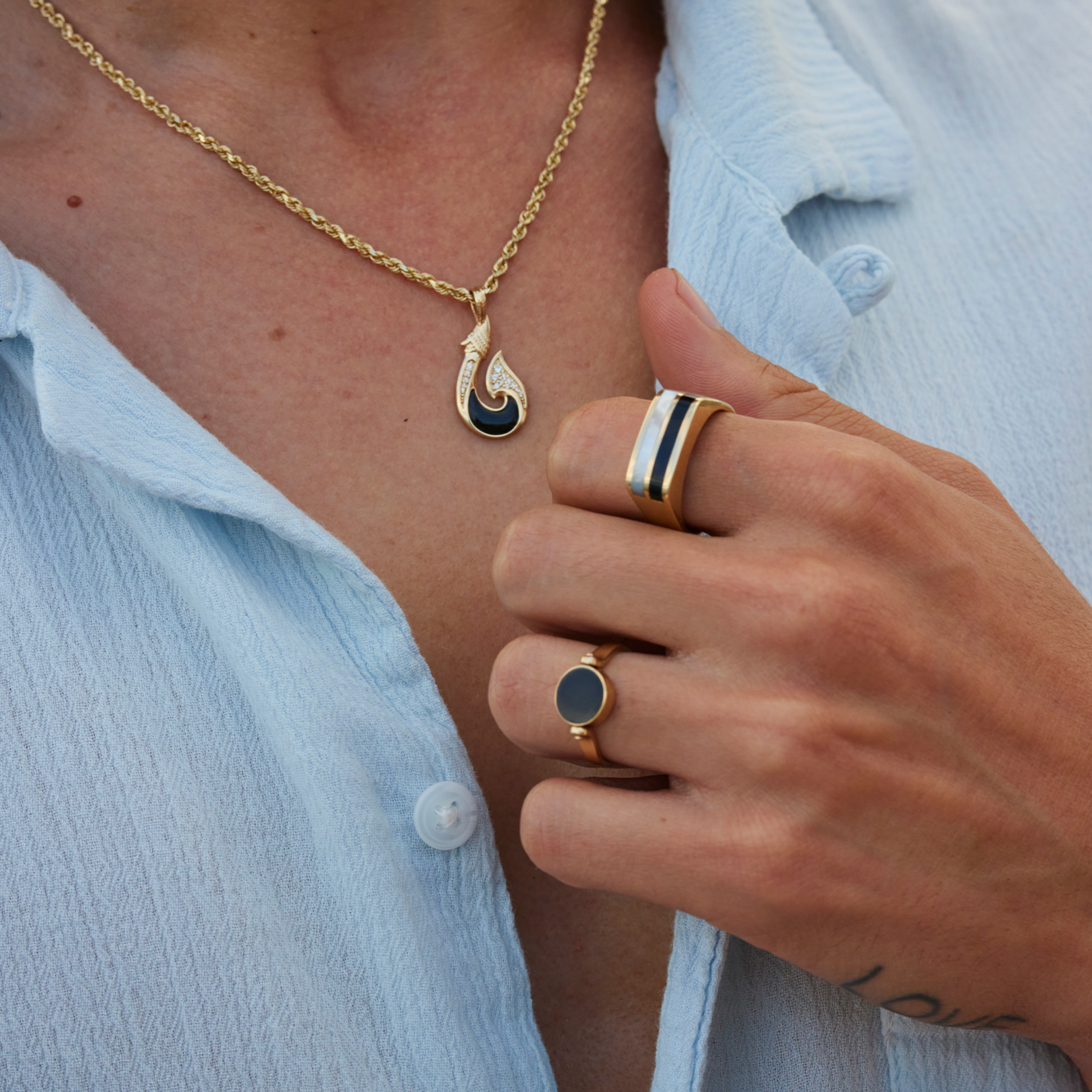 Hand holding blue shirt wearing Black Coral Ring in Gold with Mother of Pearl