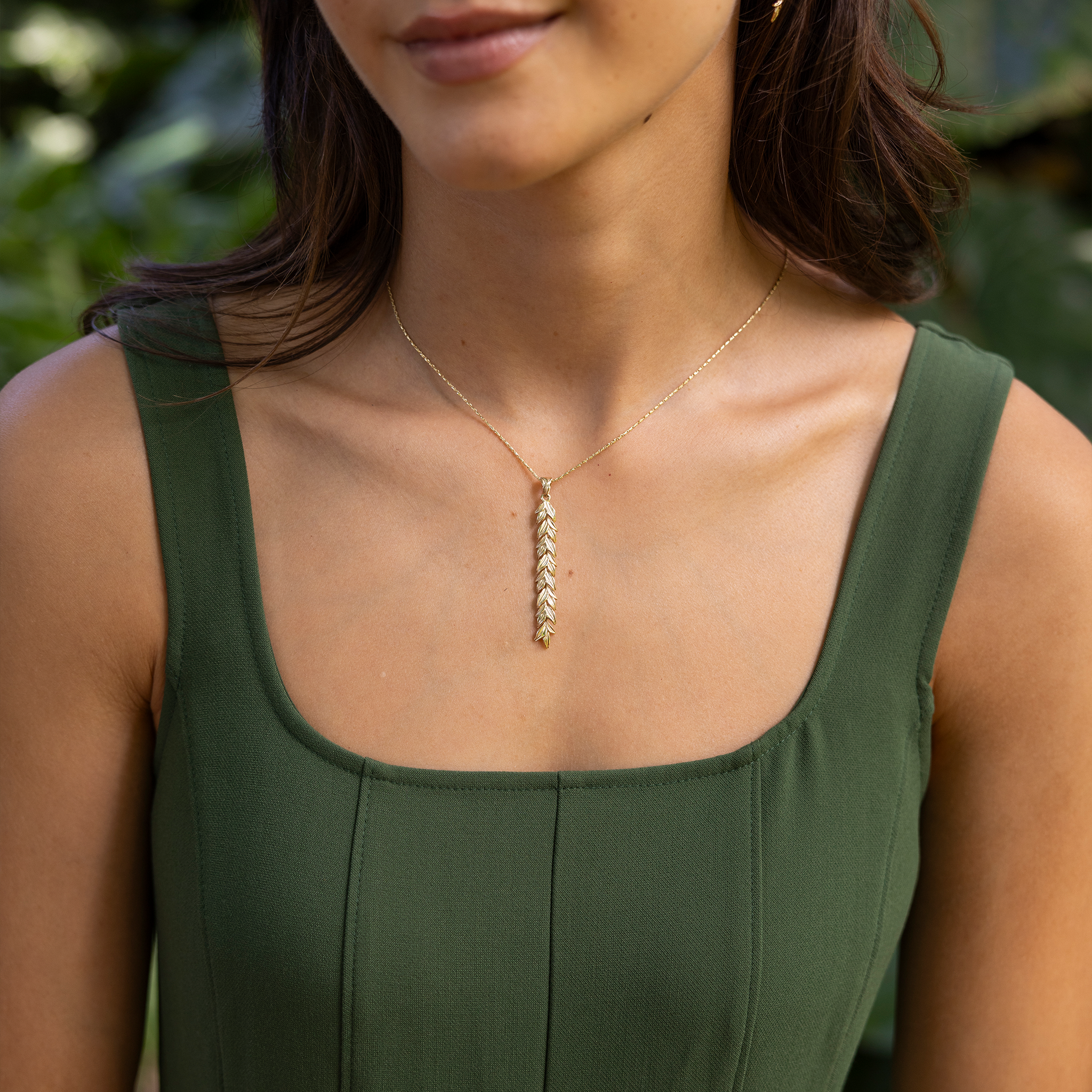 58mm Maile Pendant in Gold on a woman's chest with a garden blurred in the background