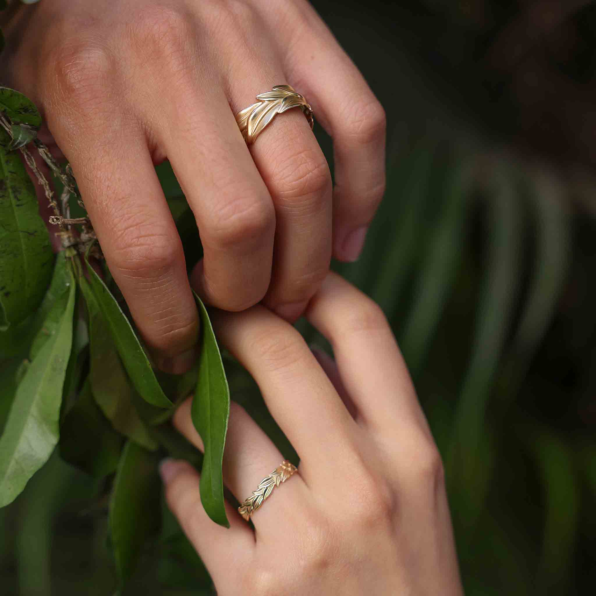 4.5mm and 10mm Maile Rings in Gold on two holding hands against a maile lei