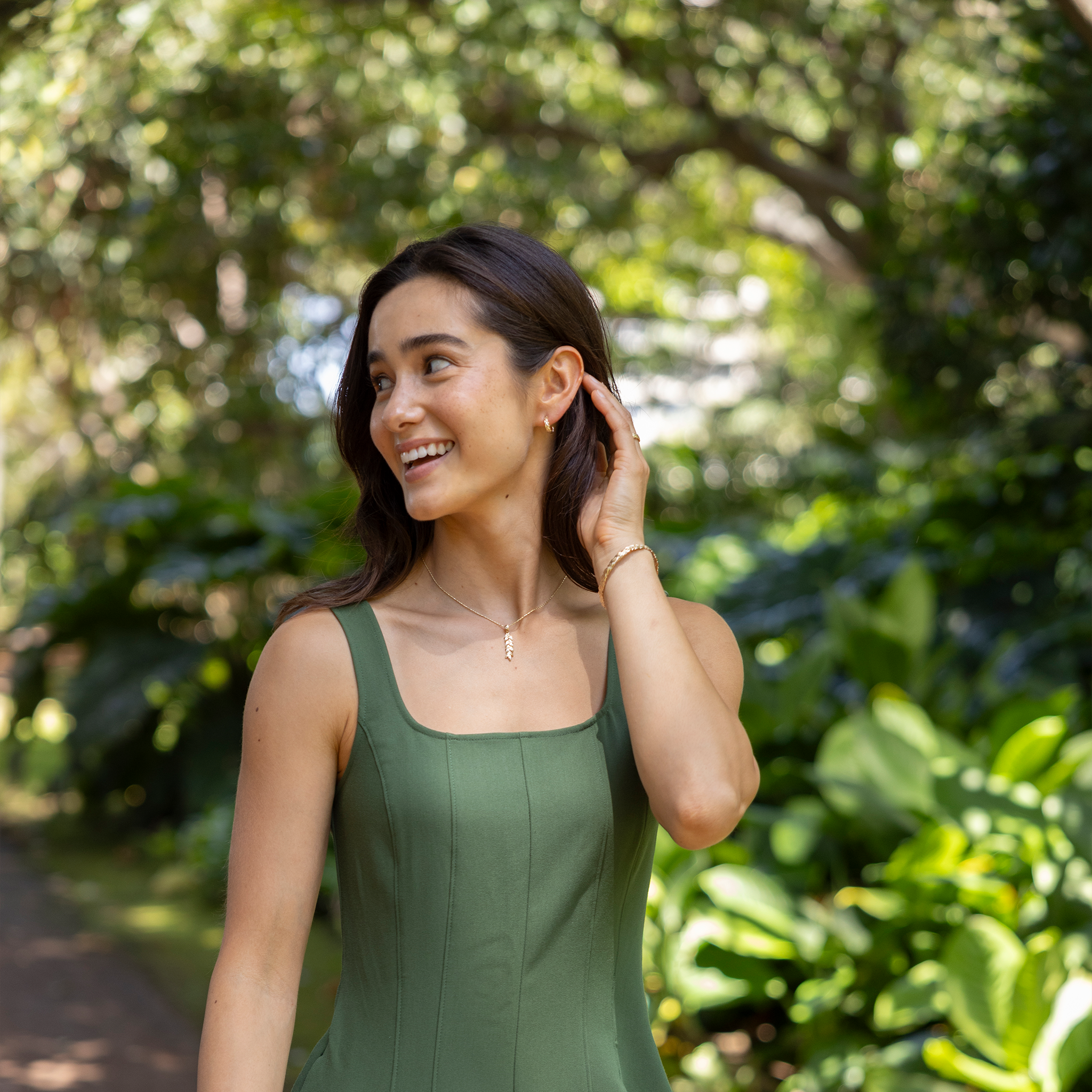 Woman in a garden wearing a 35mm Maile Pendant, bangle and earrings in Gold