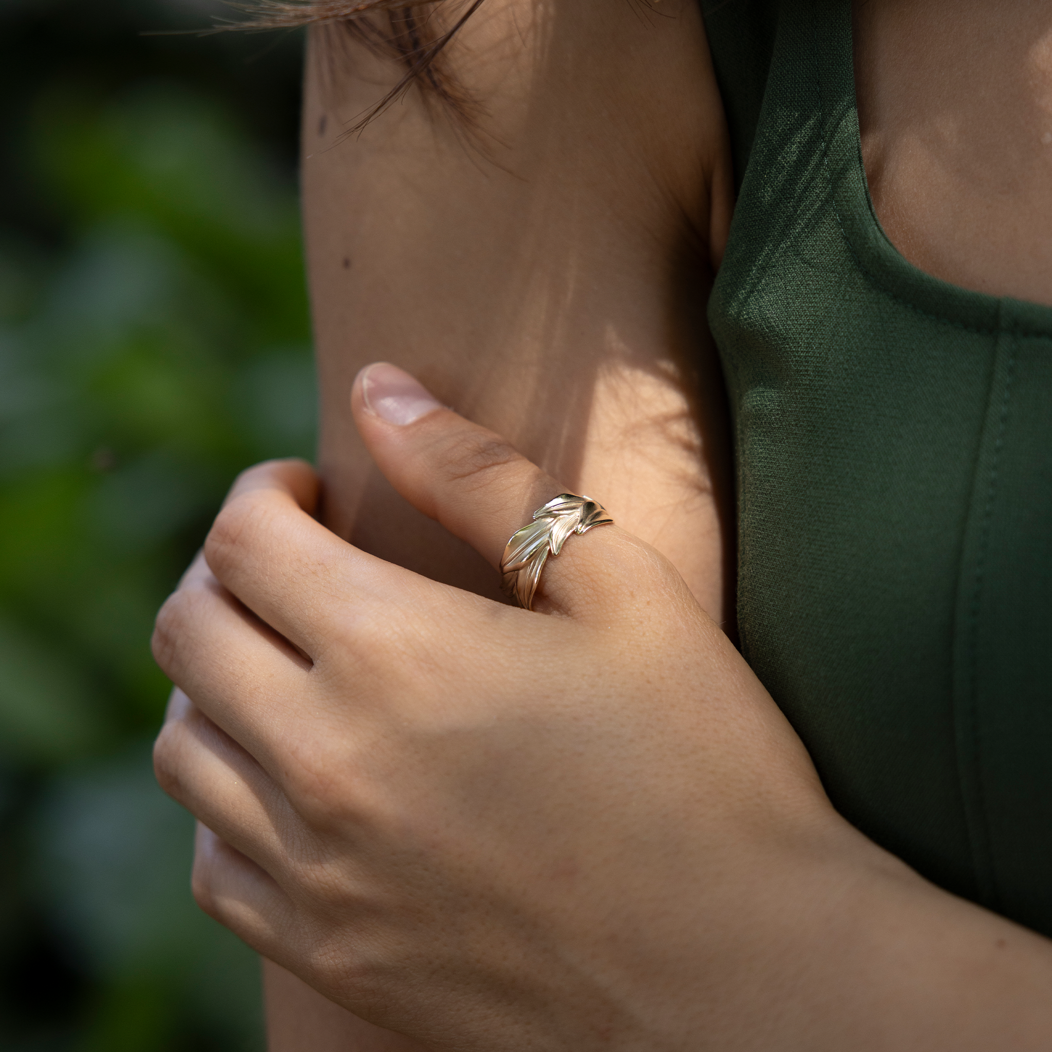 10mm Maile Ring in Gold on a hand with a blurred green background