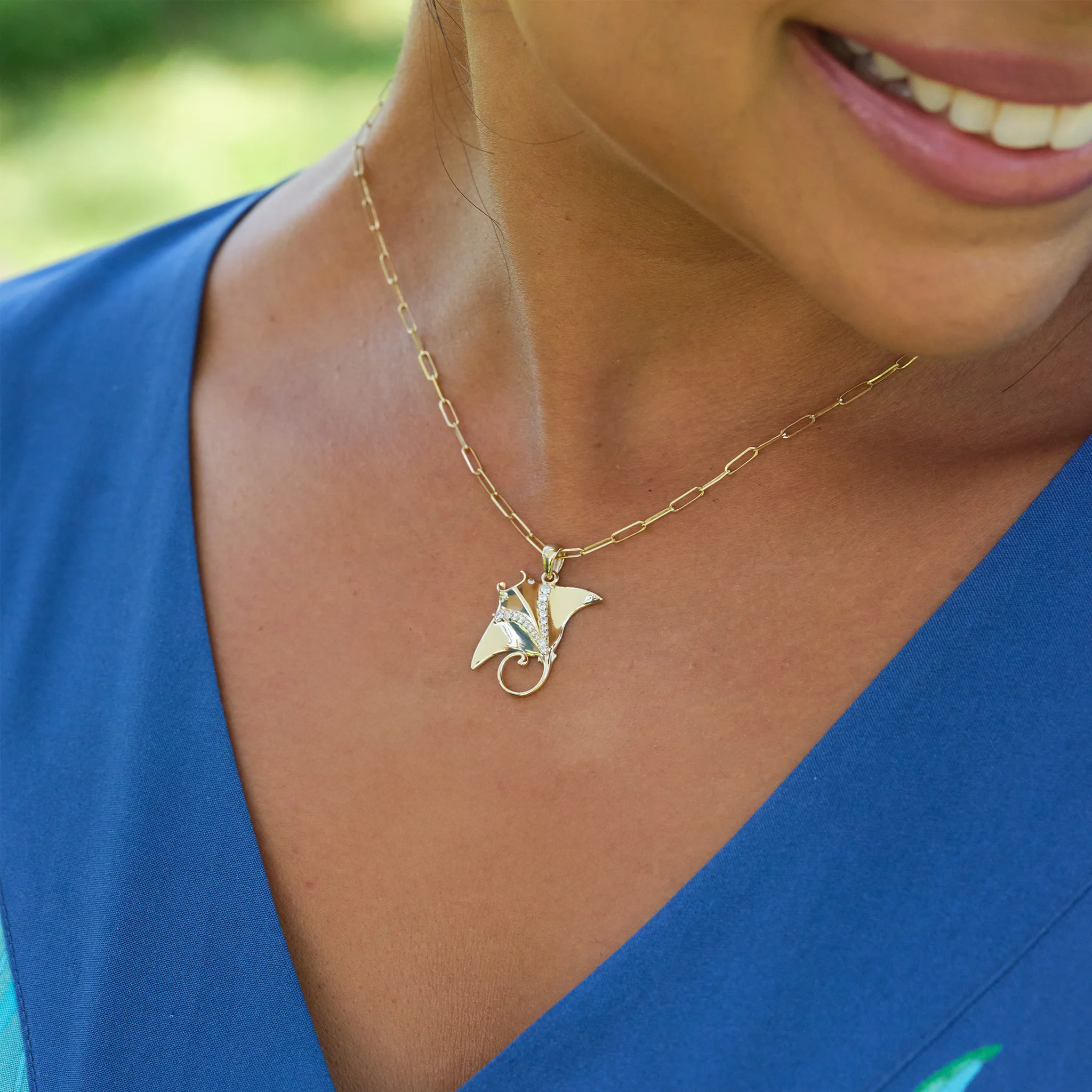 Woman wearing a blue top and an Ocean Dance Manta Ray Pendant in gold with diamonds on a paperclip chain