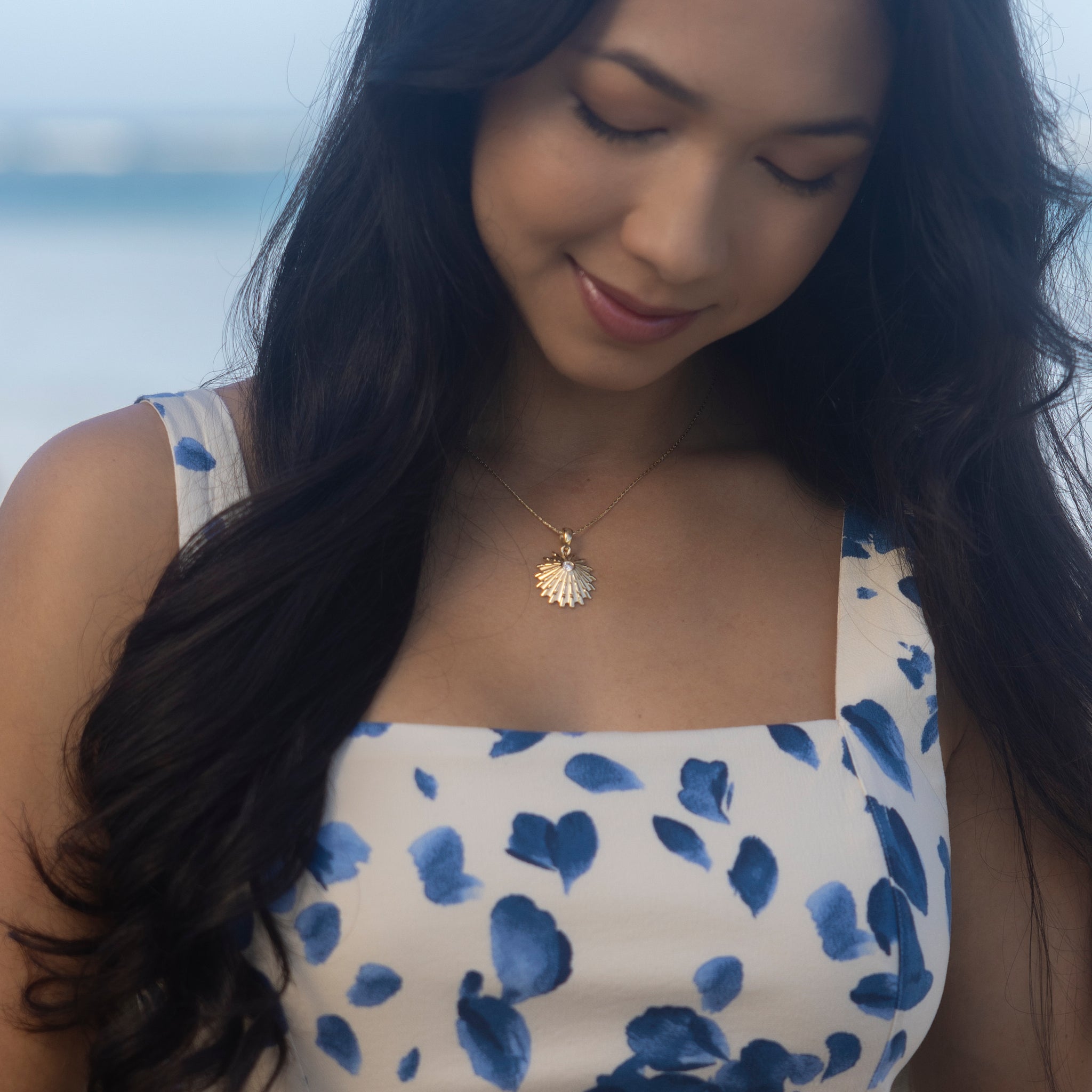 Woman wearing an ʻOpihi Pendant in Gold with Lab Grown Diamond with light blue sky in back