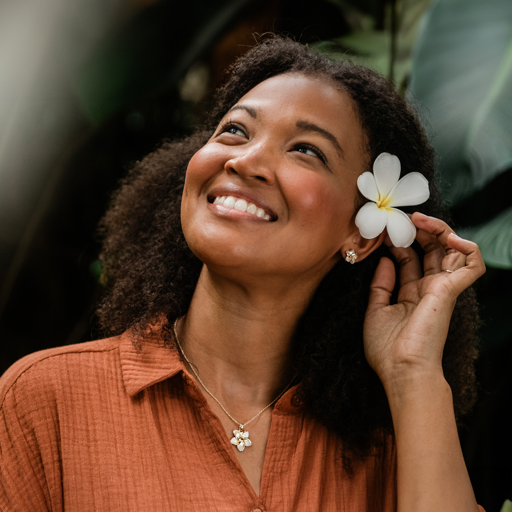 Woman in a tropical garden wearing Plumeria Mother of Pearl Pendant and earring in 14k Yellow Gold