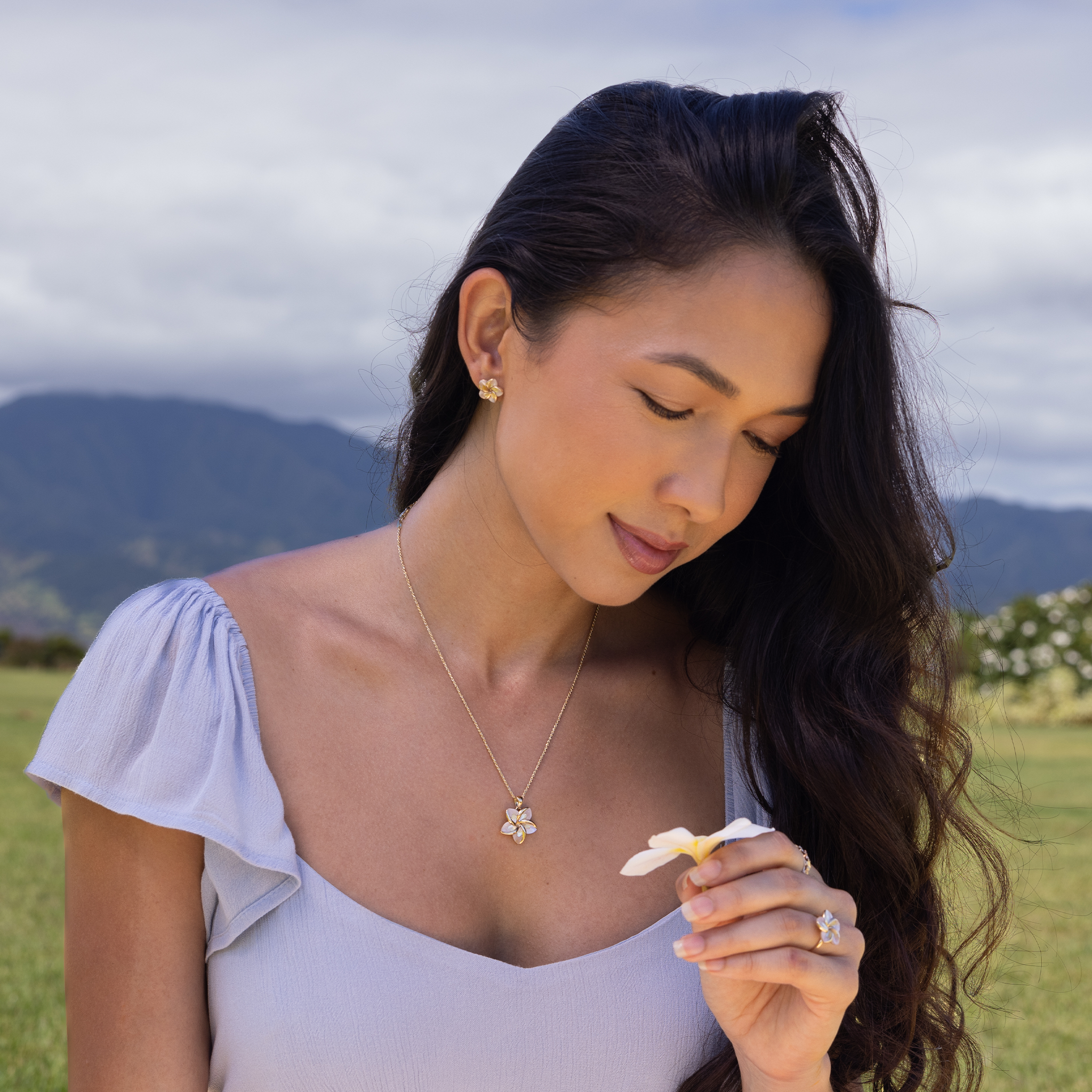 Woman sitting on lawn wearing Plumeria Mother of Pearl Pendant, ring and earrings in 14k Yellow Gold