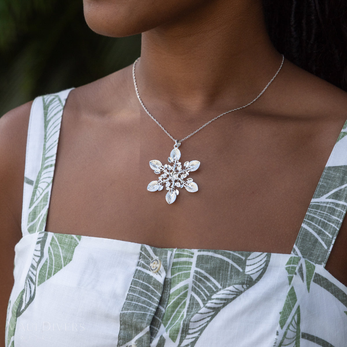 A sterling silver snowflake kalo pendant necklace worn by a model in a white and green tropical print top.