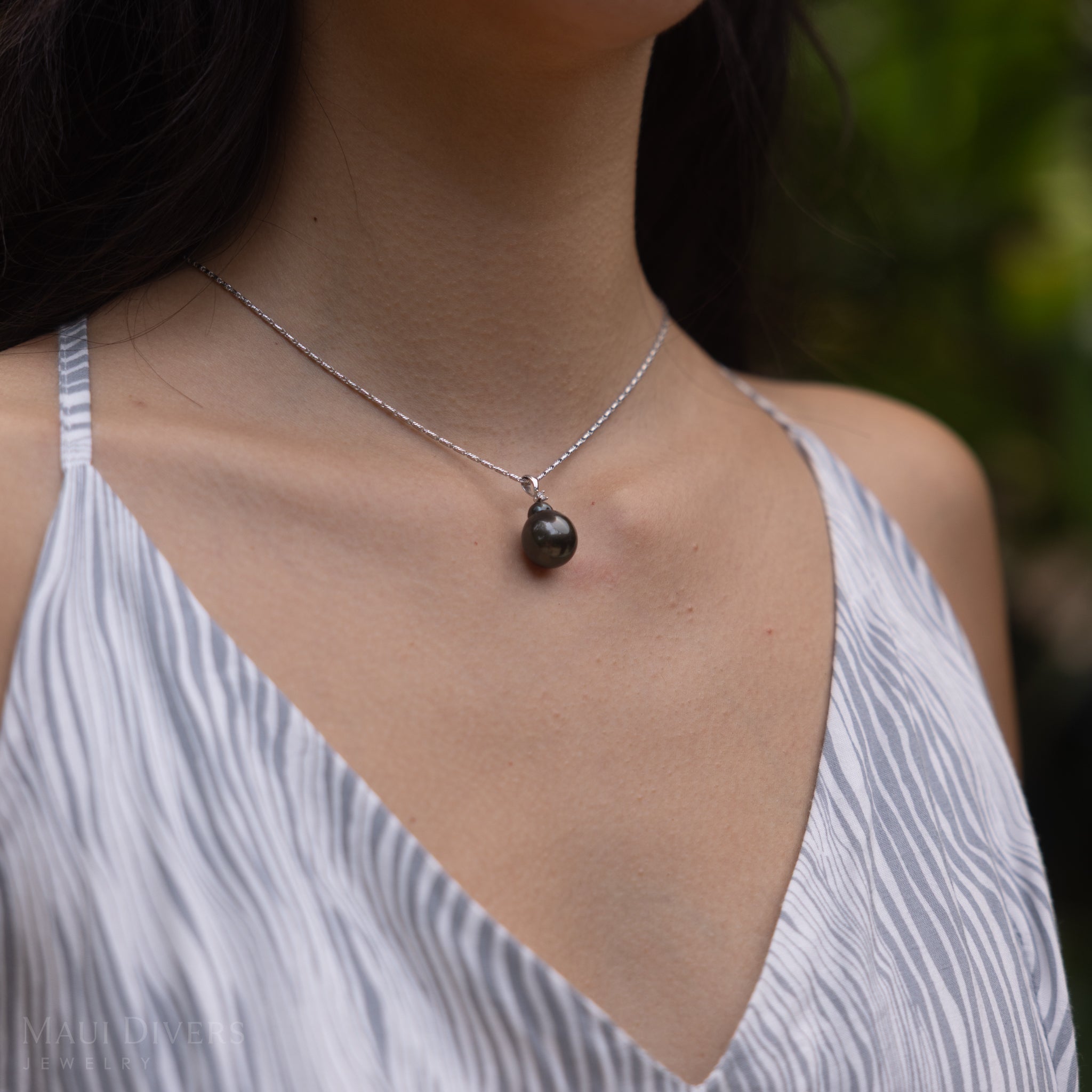 Close-up of a woman wearing a Tahitian black pearl pendant in white gold with diamond accent.
