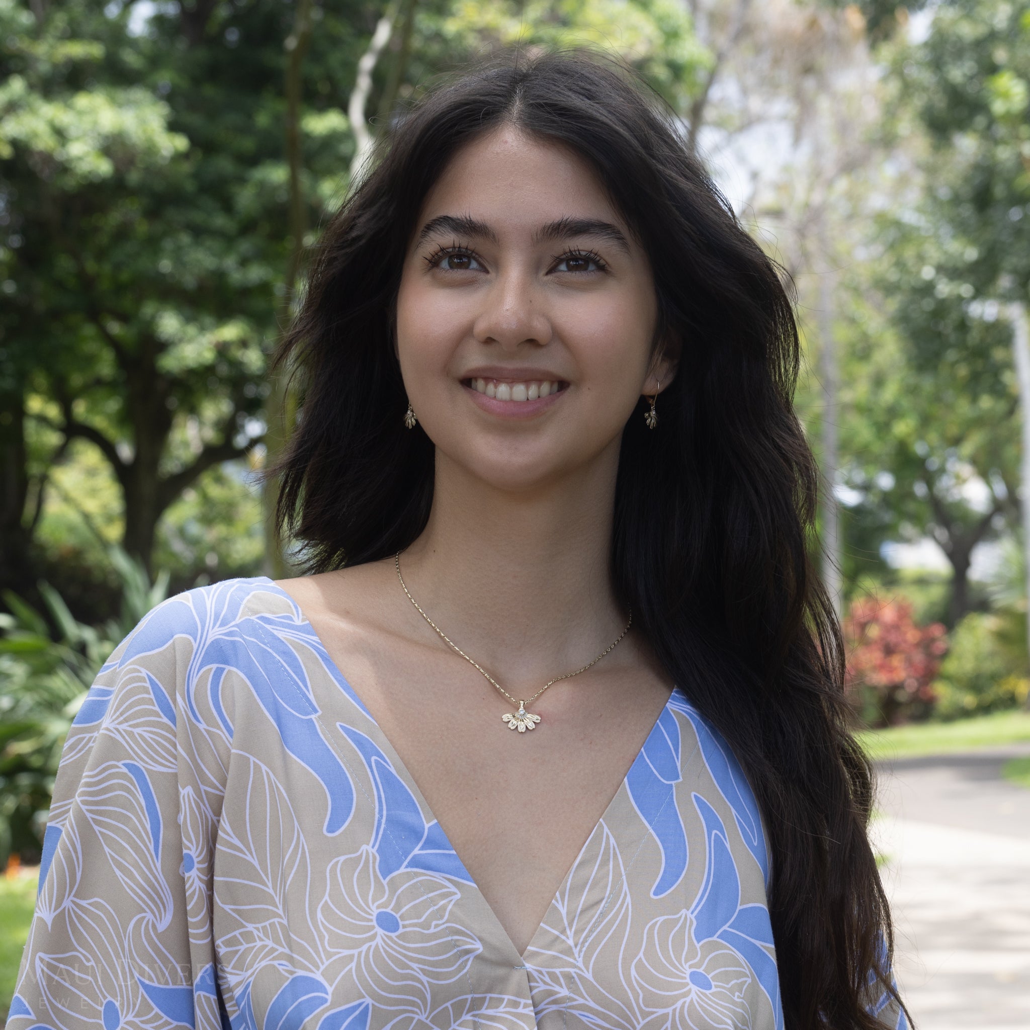 Woman in a garden wearing a Beach Naupaka Pendant and earrings in Gold with Diamonds