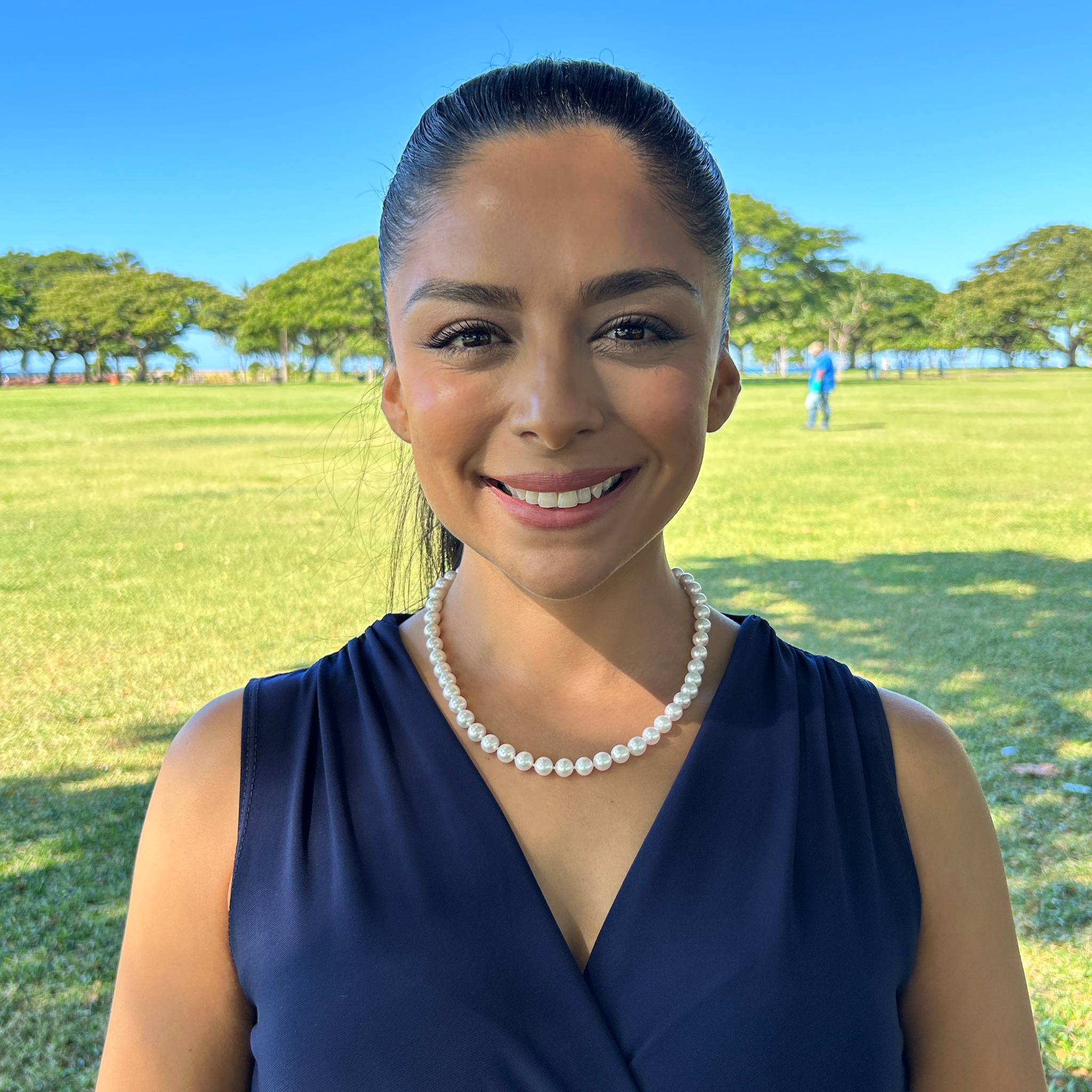 Woman smiling wearing an Akoya white pearl strand necklace in front of a blurred background
