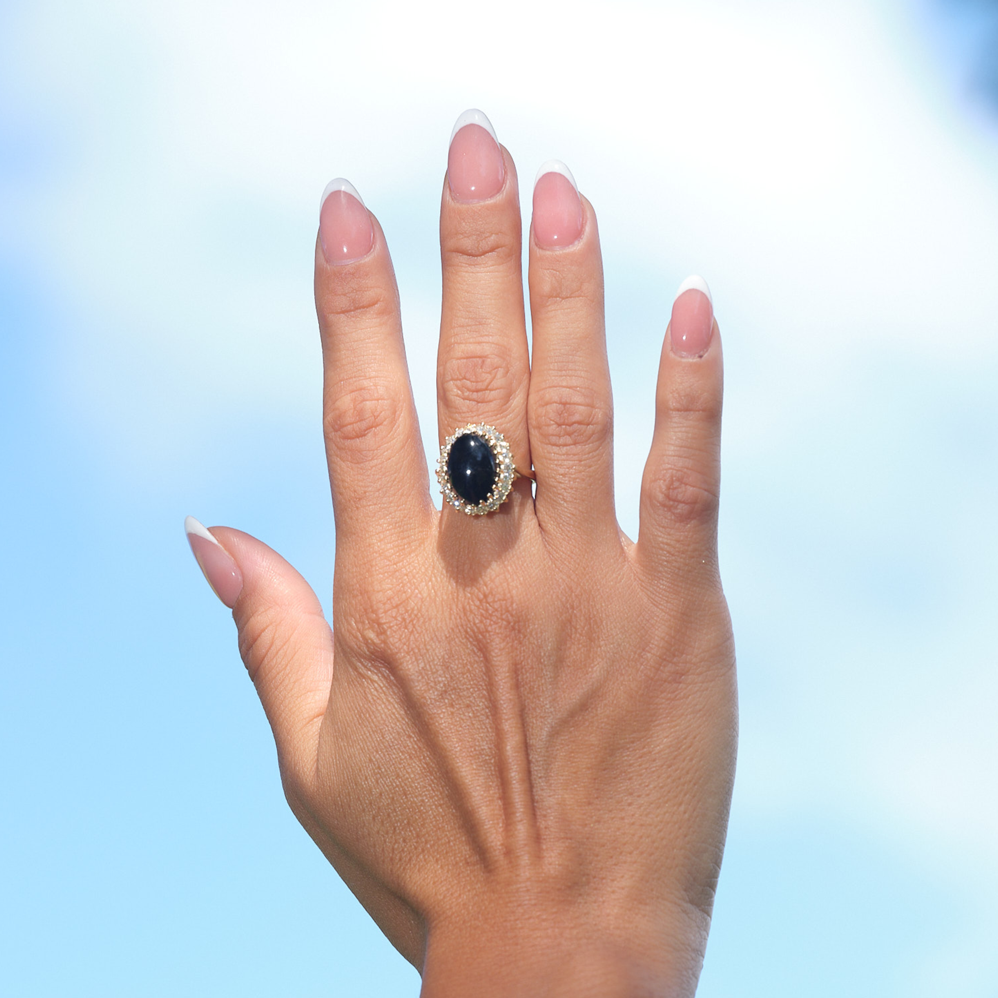 A woman's hand wearing a Princess Ka‘iulani Black Coral Ring in Gold with Diamonds against blue sky