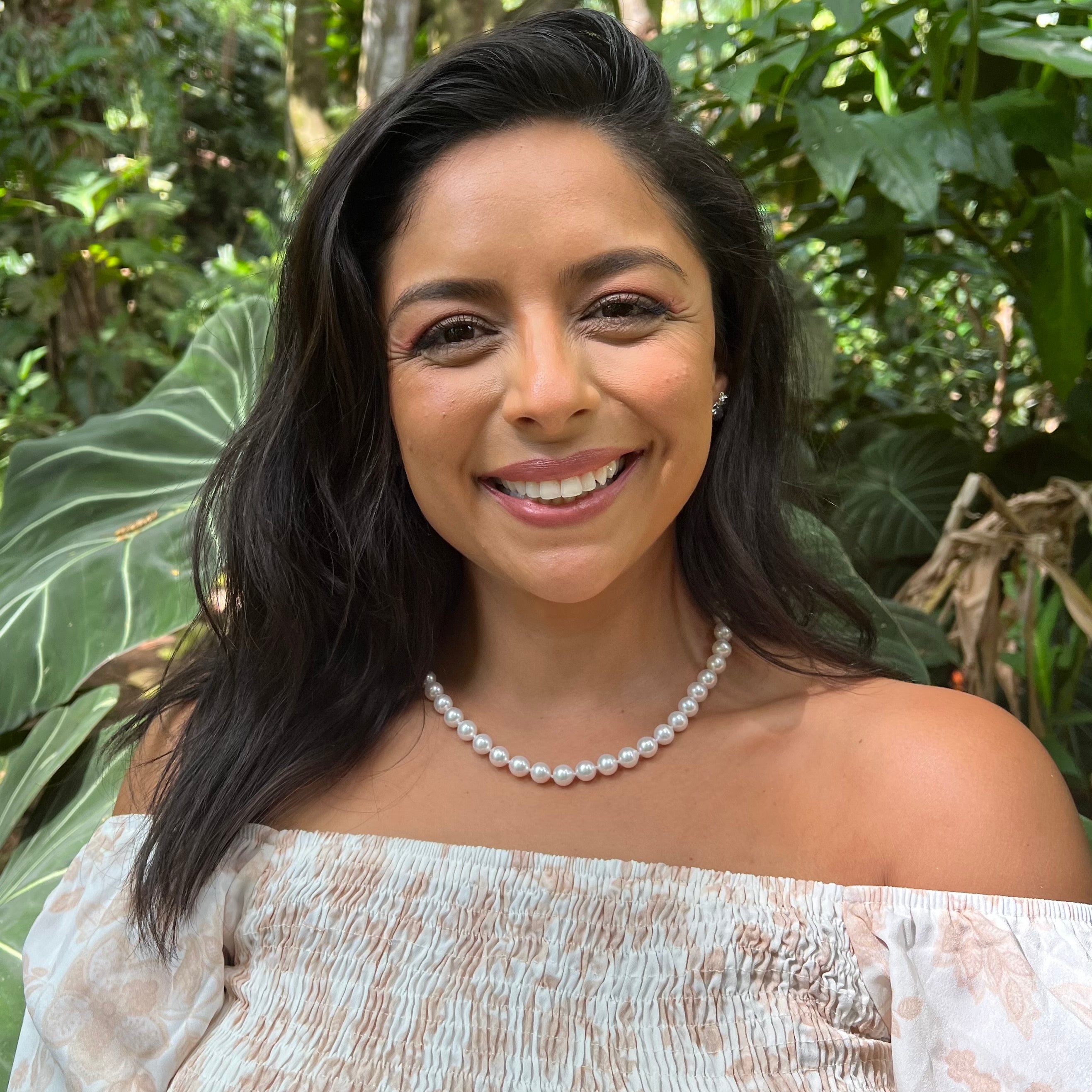 Smiling woman wearing an Akoya white pearl strand necklace in front of a blurred forest background
