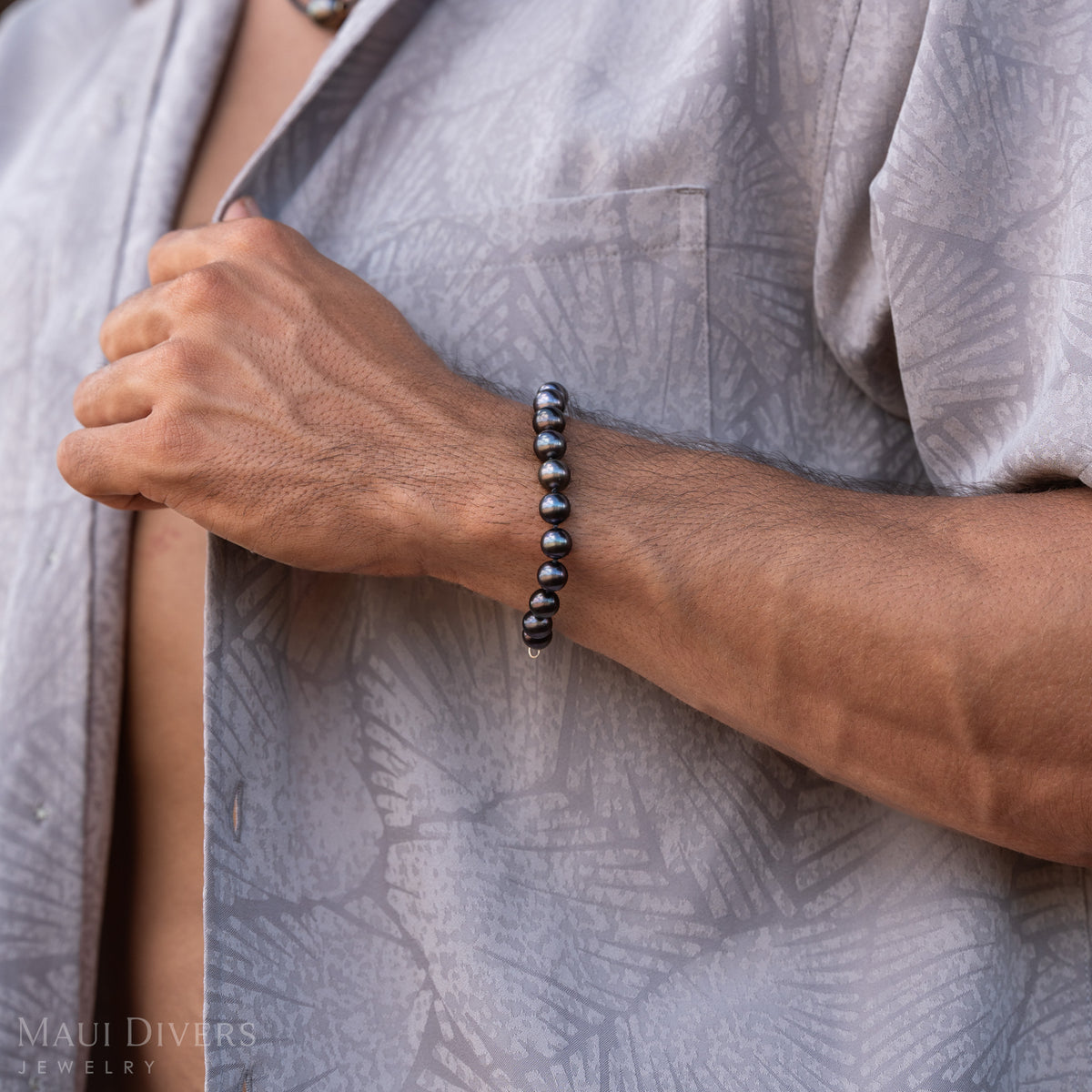Detail shot of a Tahitian black pearl necklace on a man's wrist against a patterned grey shirt