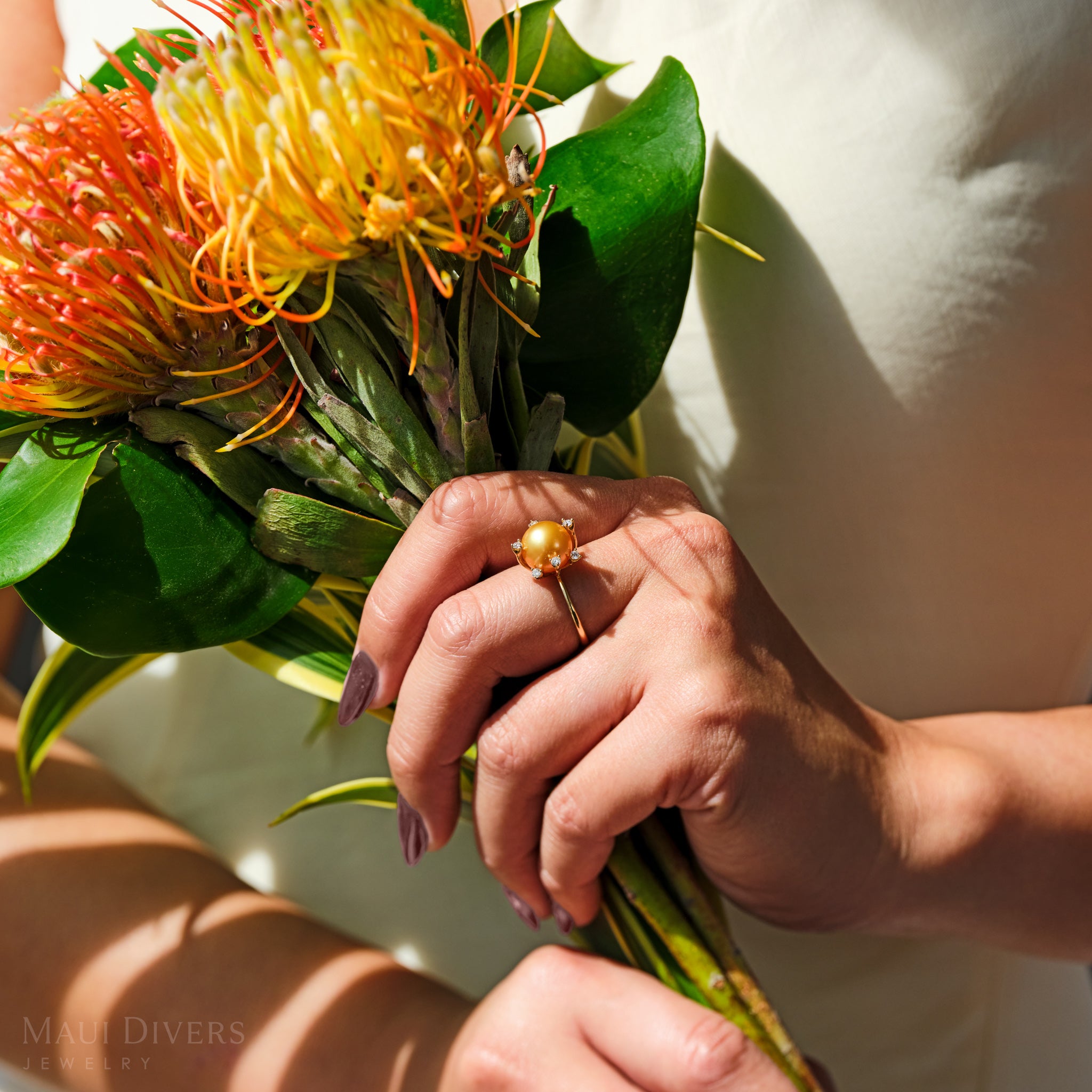 Close-up of a South Sea gold pearl ring with diamonds in 14k yellow gold worn on a hand holding a bouquet of flowers.