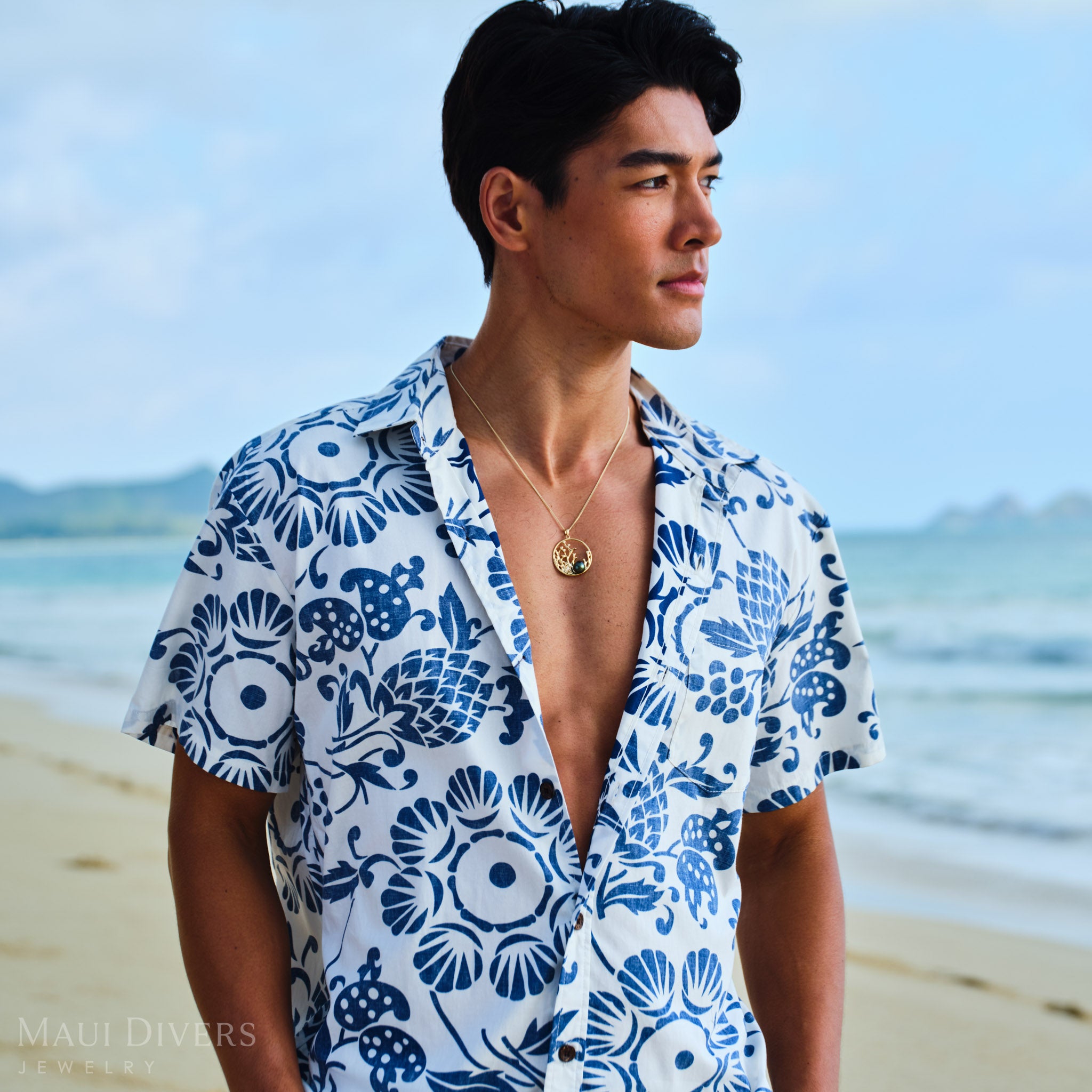 Man wearing a blue and white patterned shirt and Reefs Tahitian Black Pearl Pendant in Gold on a beach
