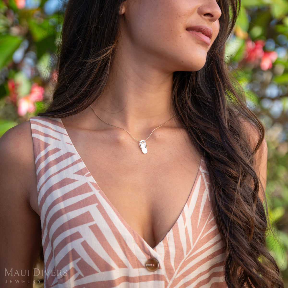 Woman with a neckline showing a White Mother of Pearl Slipper Pendant with 14k Gold details with a pink and green nature background. 