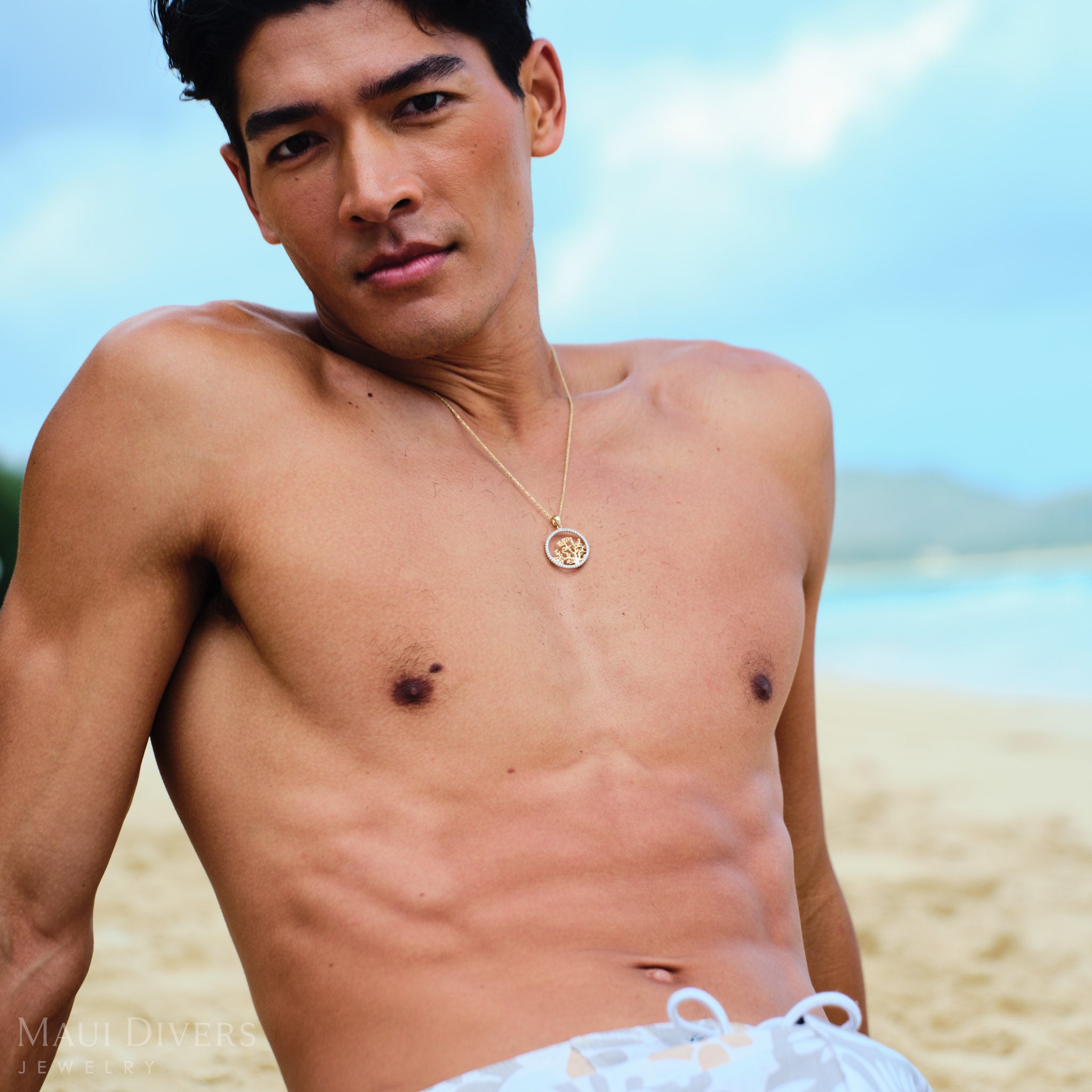 Man leaning back on a beach wearing a two-toned gold coral branch pendant with diamonds