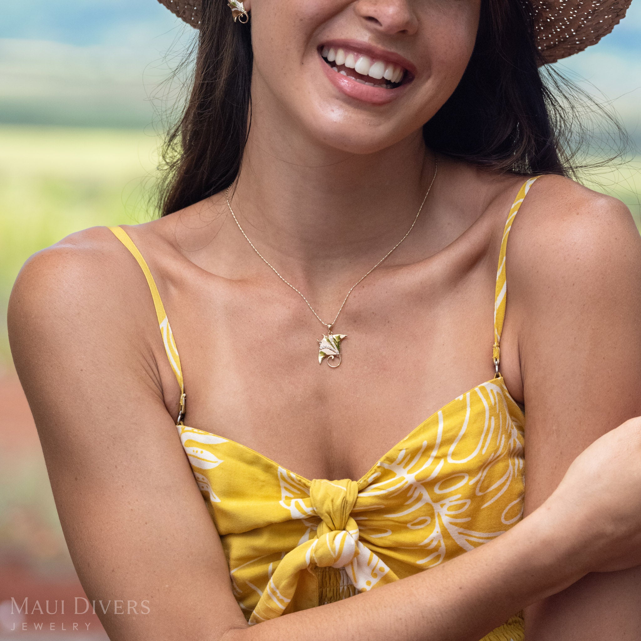 Woman smiling with one arm crossed in front of her wearing a 14k Gold Manta Ray Pendant around her neck with Natural Diamond detailing. 