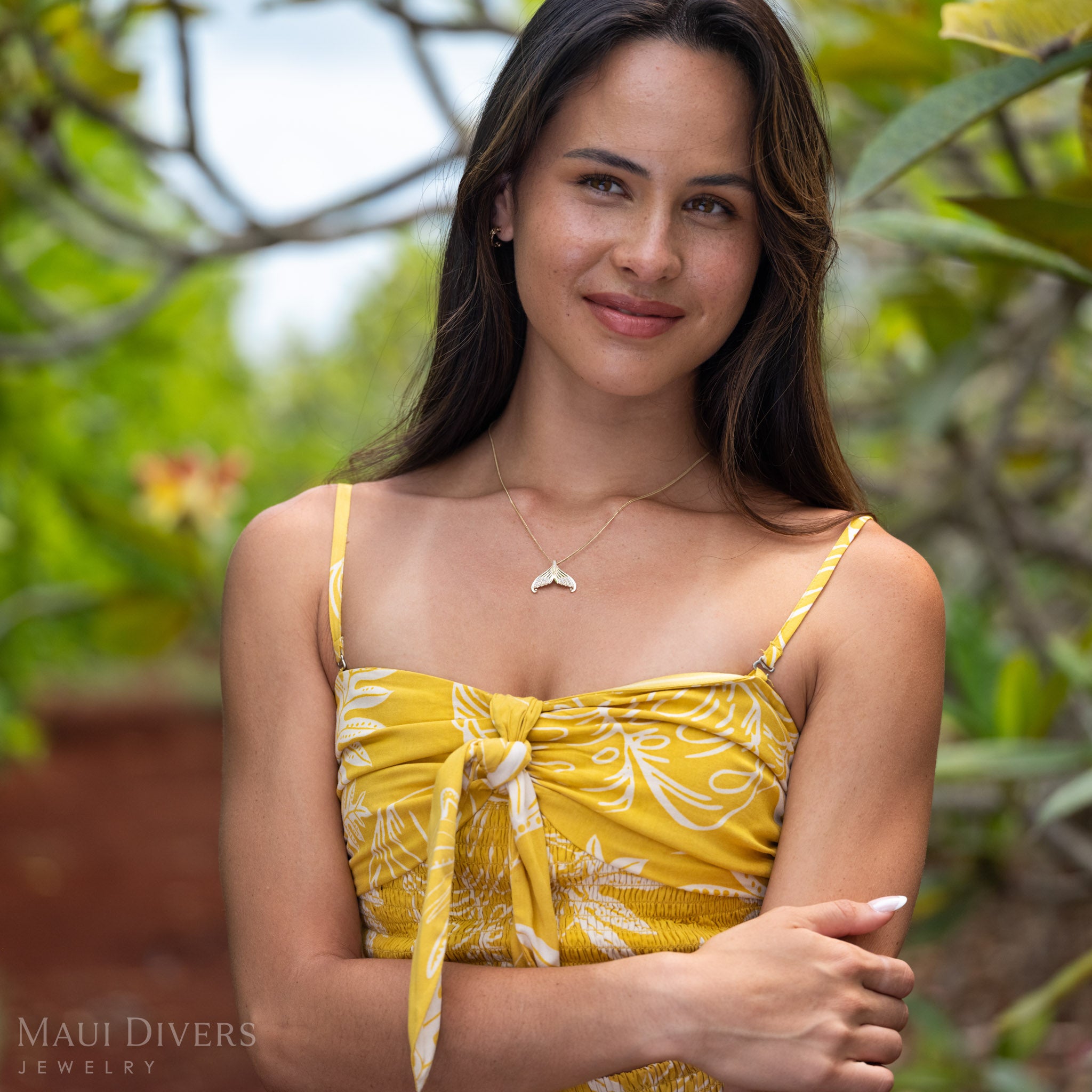 Woman wearing a 14k Gold Mermaid Tail Necklace with Natural Diamond accents and a yellow knotted top against a green natural background. 