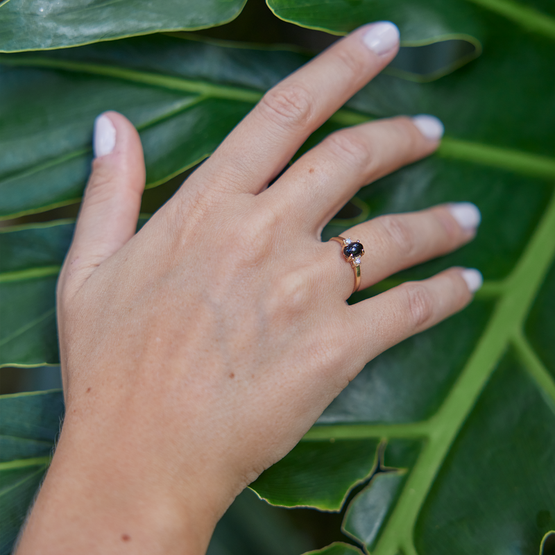 Womanʻs hand wearing Black Coral Ring in Gold with Diamonds as she touches a leaf