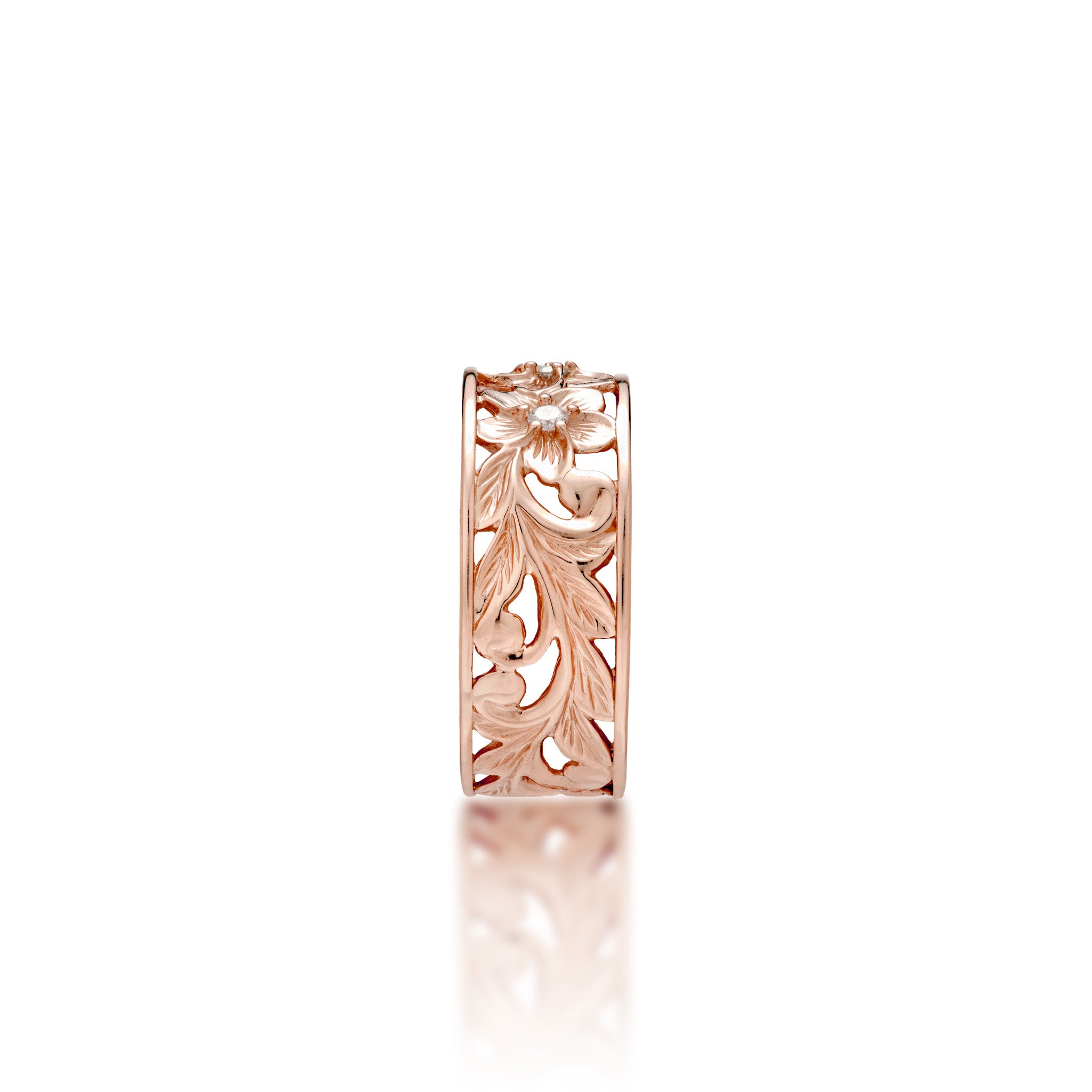 A side view of a 14k rose gold Hawaiian Heirloom ring with an intricate fern and maile leaf scrollwork pattern featuring plumeria flowers at the top with diamond accents, shown on a clean white background with a soft reflection.