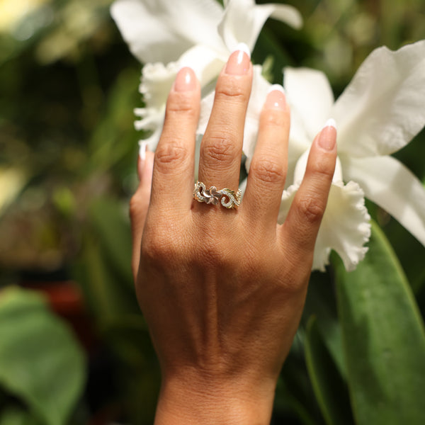 Close up of hand wearing Hawaiian Heirloom Plumeria Ring in Two Tone Gold with Diamonds while touching white flower