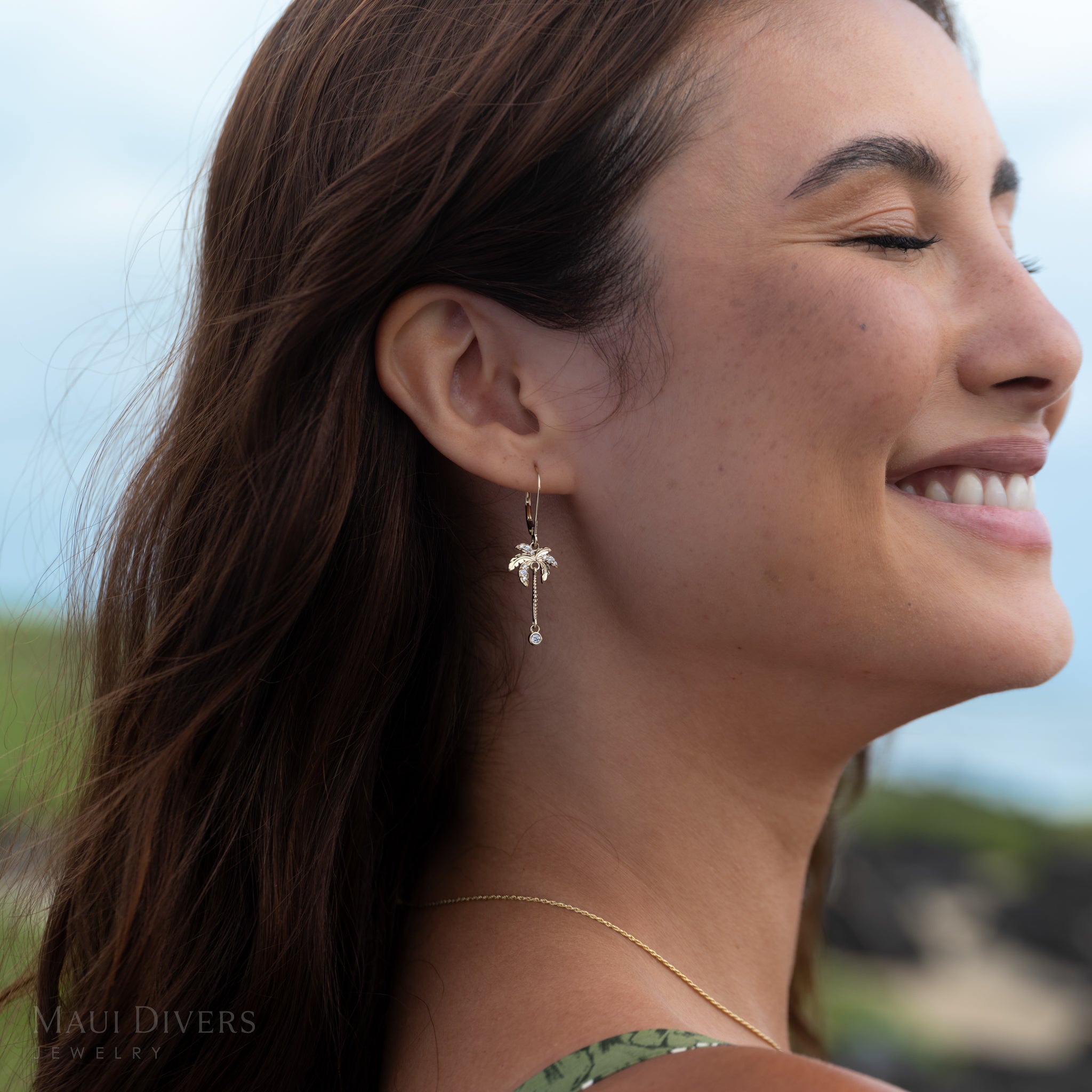 Close-up of a smiling woman wearing a gold and diamond palm tree earring