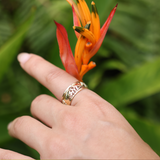 A woman's hand with a Hawaiian Gardens Monstera & Heliconia Ring in Tri Color Gold - 8mm holding a flower - Maui Divers Jewelry