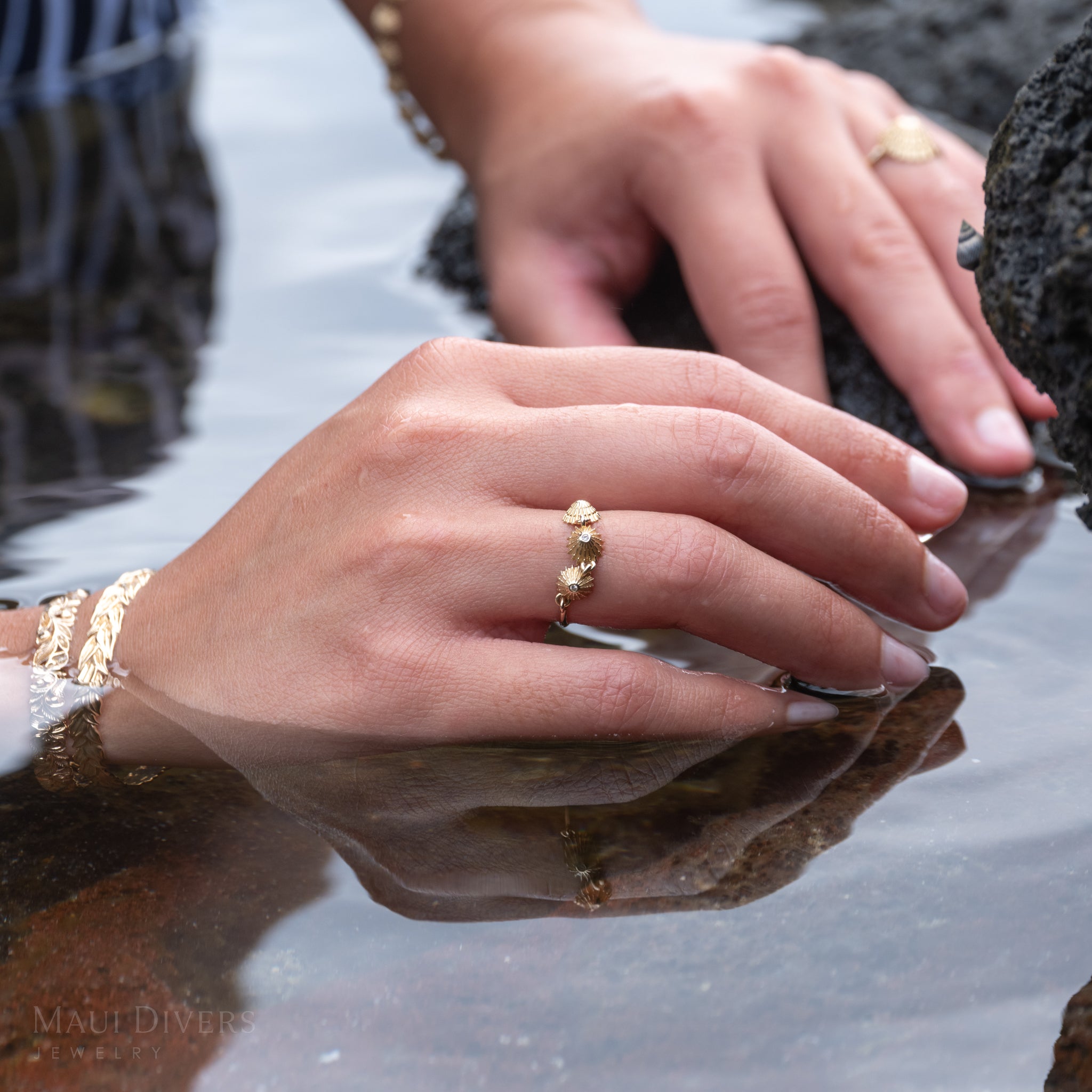Close-up of a hand in water wearing the 6mm gold and diamond ʻopihi ring