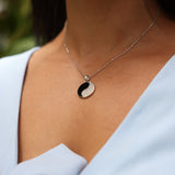 Close up of woman wearing Yin Yang Black Coral Pendant in White Gold with Diamonds - 19mm with blue dress framing neckline
