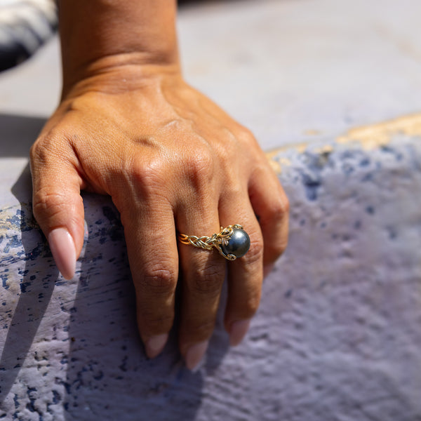 Tahitian Black Pearl Ring with Ornate Design in Gold  on Finger with cement background - Maui DIvers Jewelry