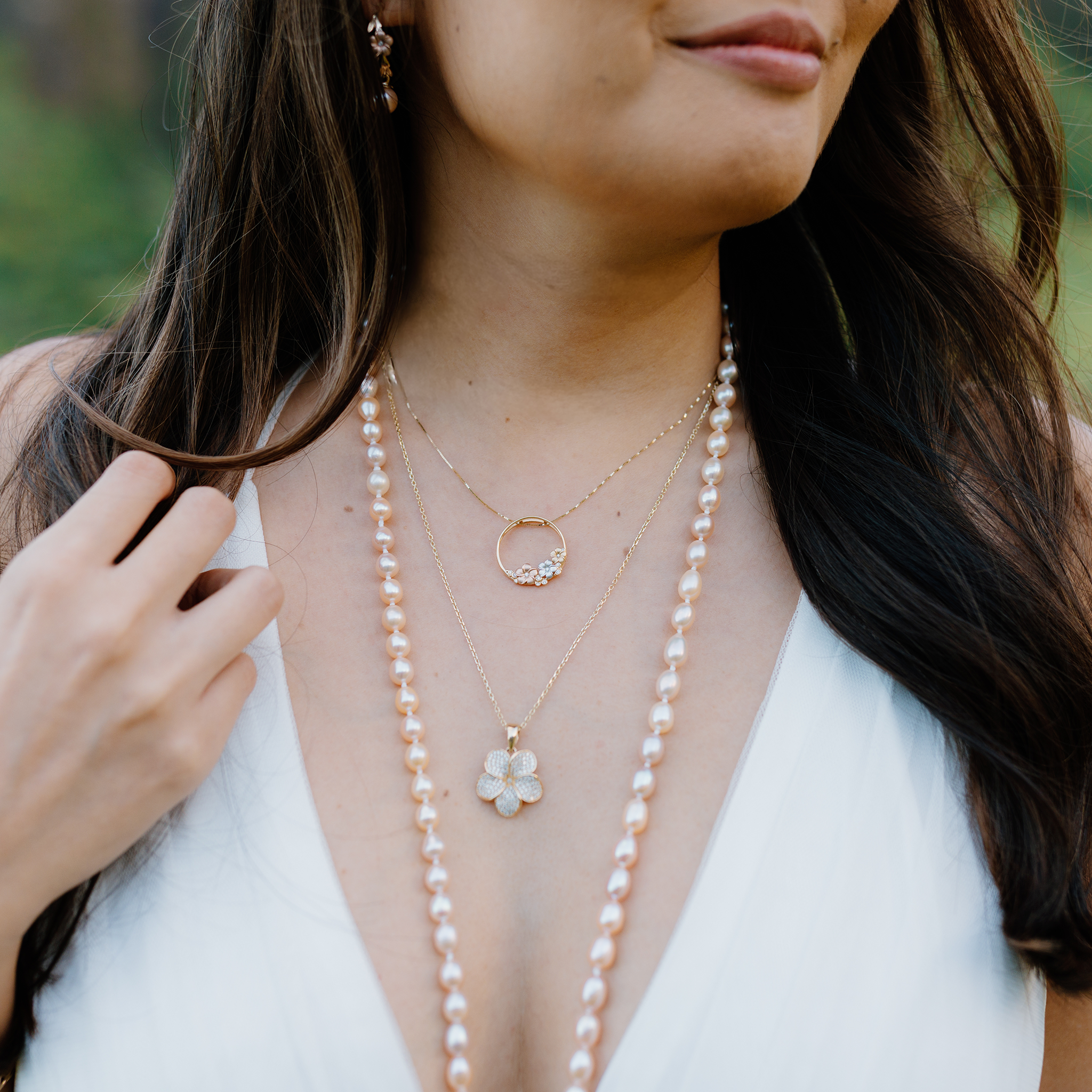 Woman wearing a long pearl necklace and two plumeria necklaces with a white top outdoors