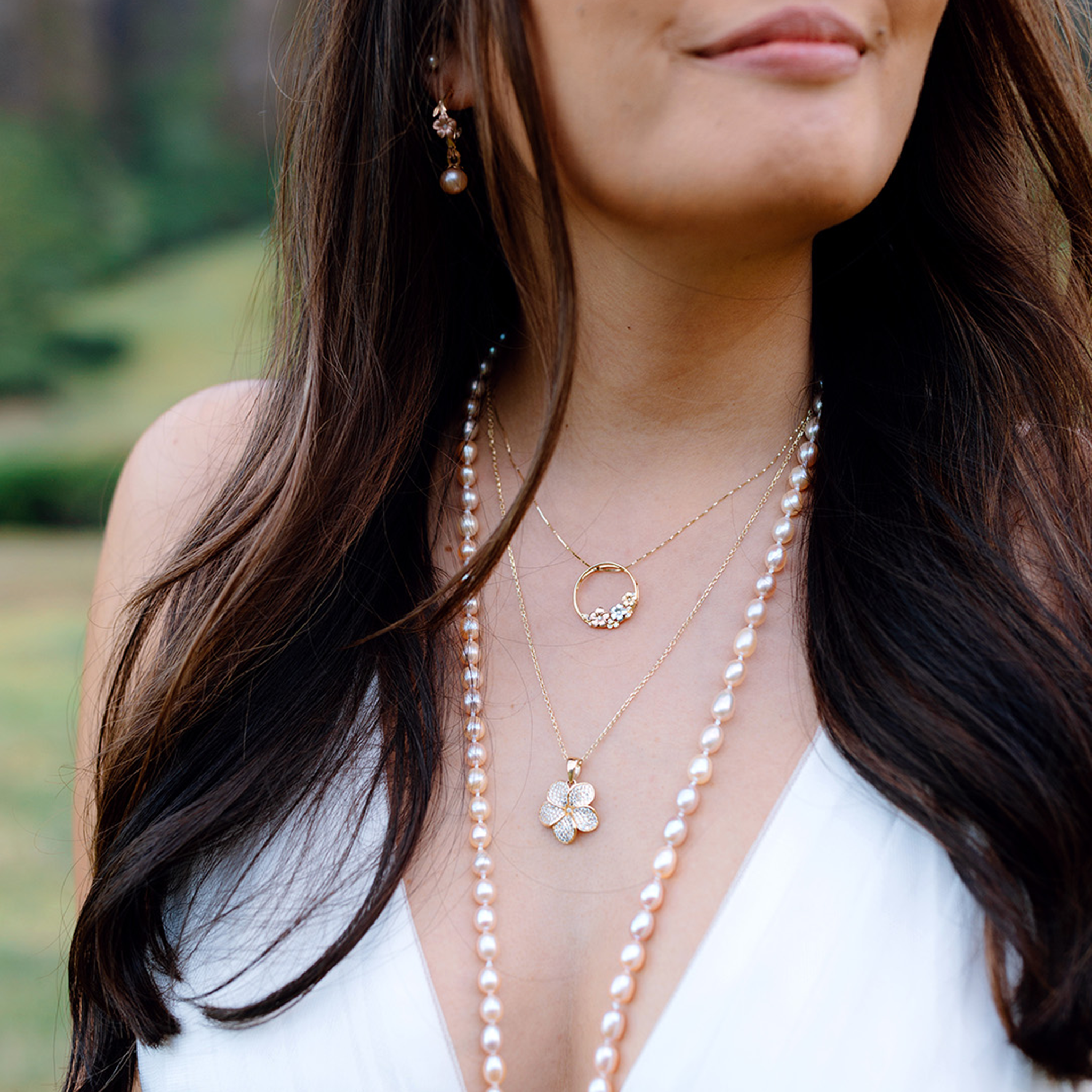 Close-up of a woman wearing pearl necklace and plumeria diamond pendants with a blurred natural background