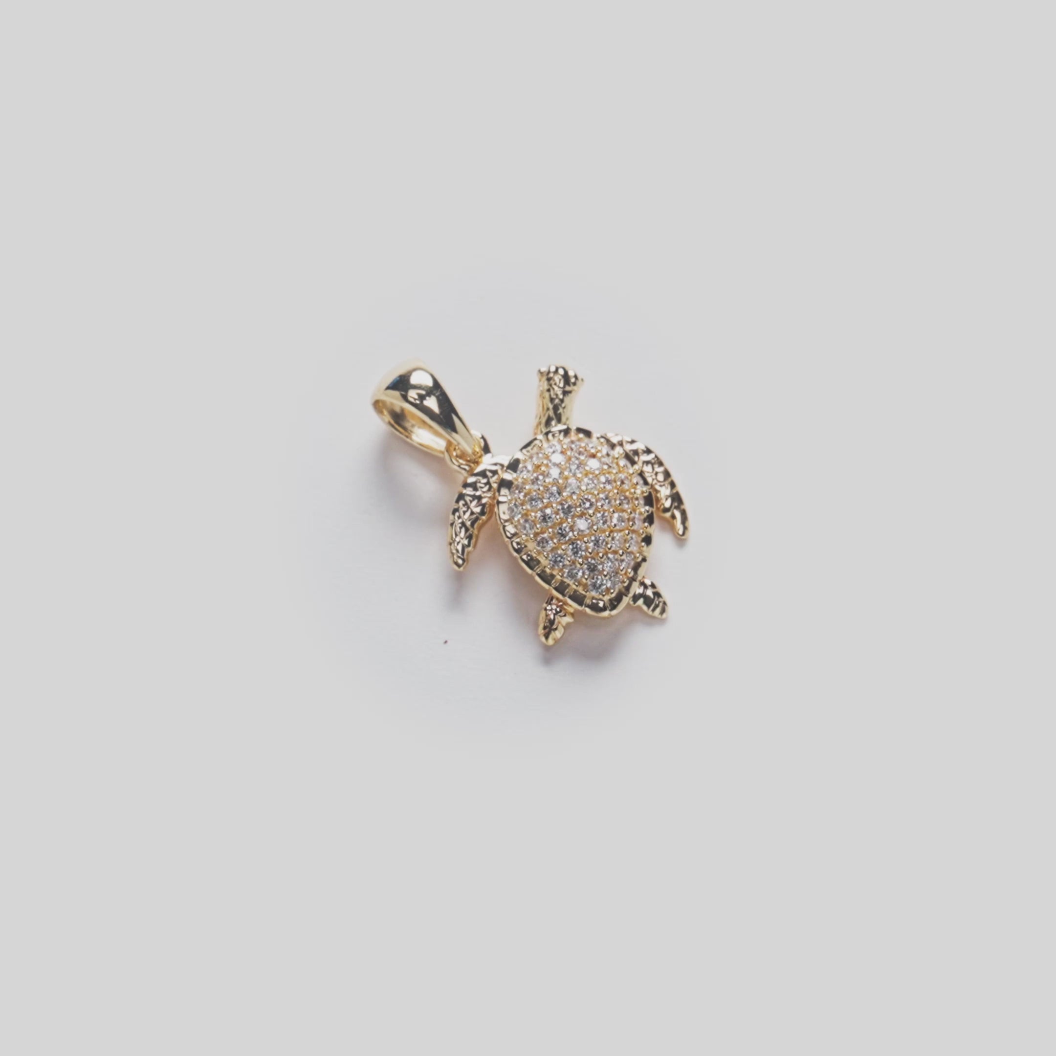 Video showing detail of diamonds on gold turtle pendant on white turn table
