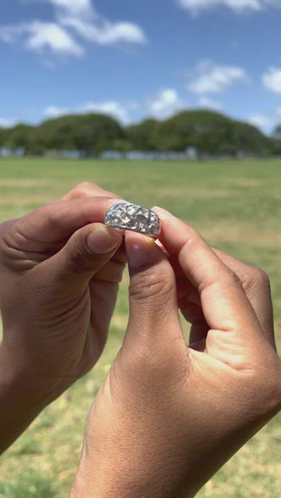 Video of a woman's hand holding a Hawaiian Heirloom Plumeria White Sapphire Ring in Sterling Silver by Maui Divers Jewelry in a grassy field.	