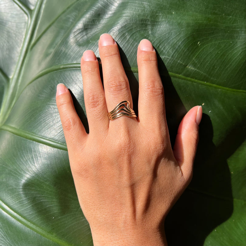 A woman's hand wearing a Nalu Ring in Gold on a leaf background- 11mm - Maui Divers Jewelry